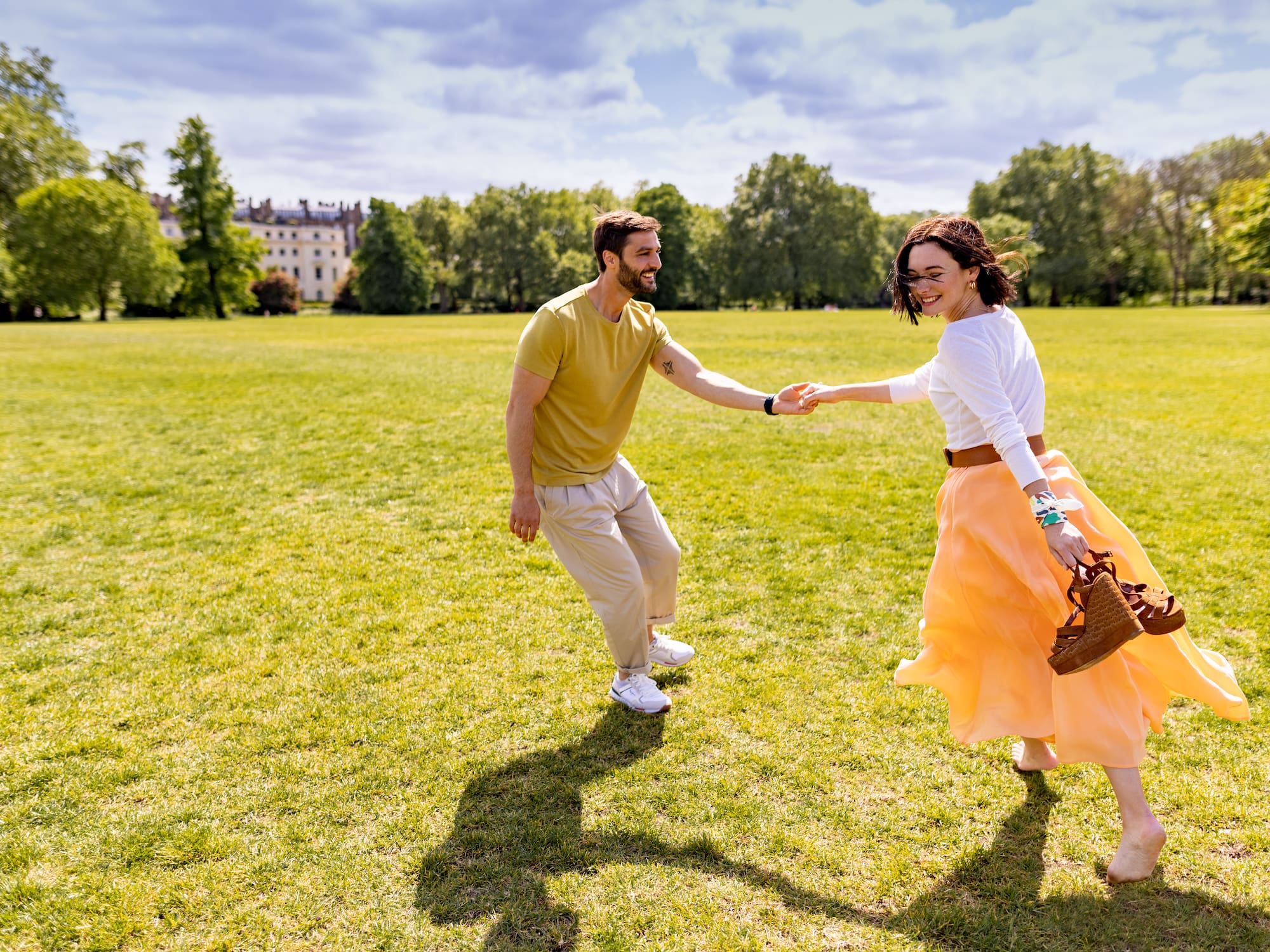 A man and woman are running together, hand in hand, across a field.