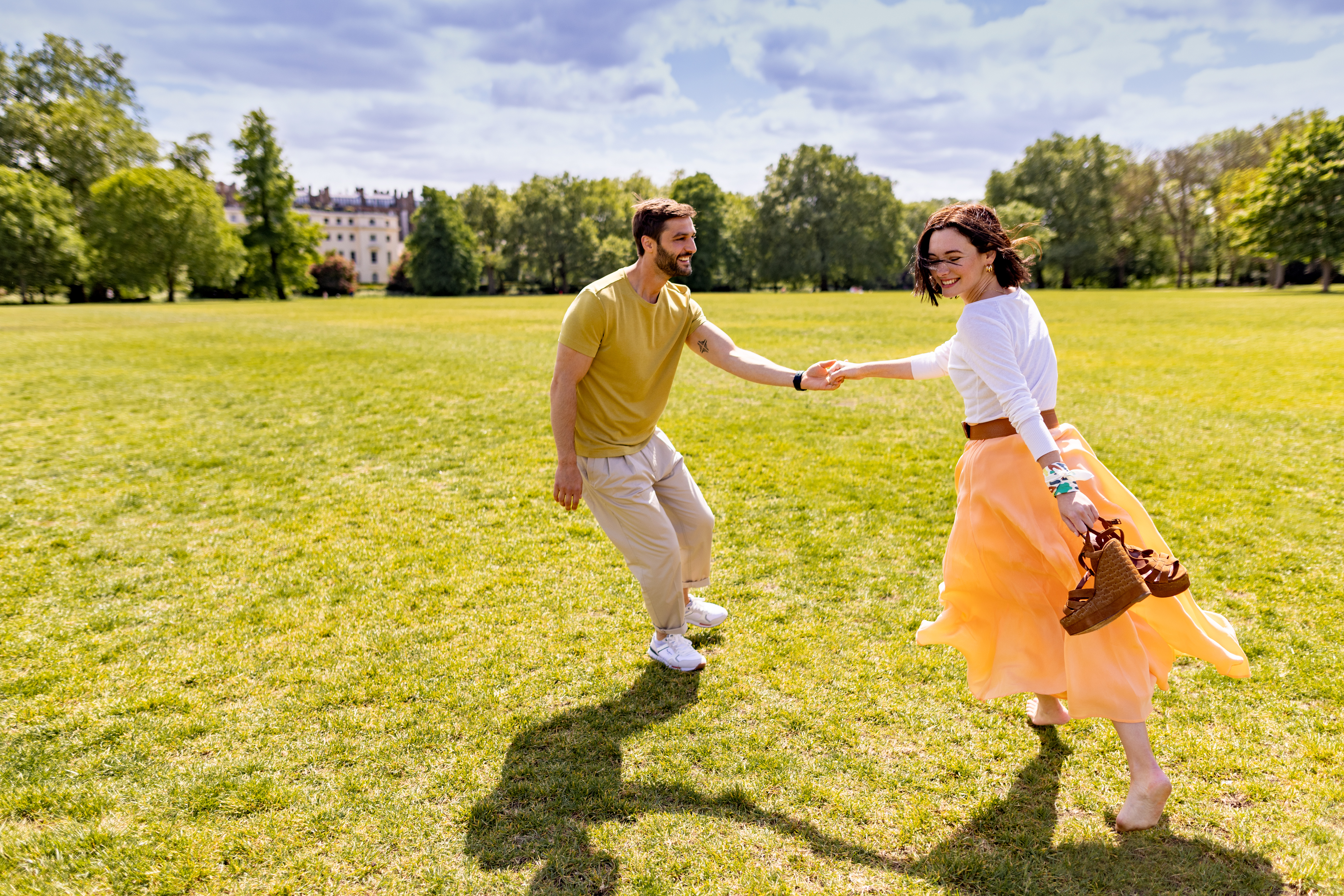 A man and woman are running together, hand in hand, across a field.