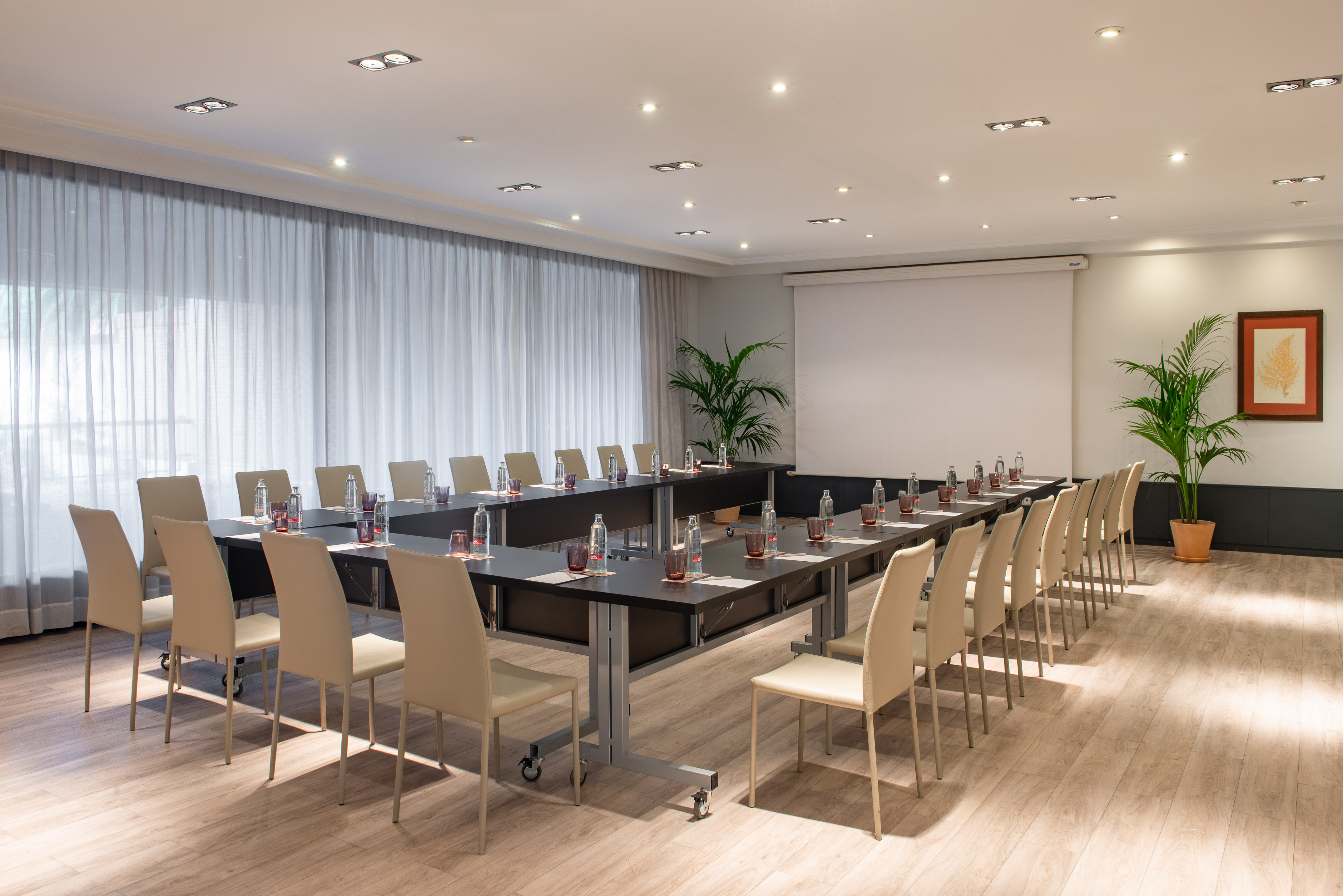 U-shape conference room with tables, chairs, water bottles, and presentation screen.