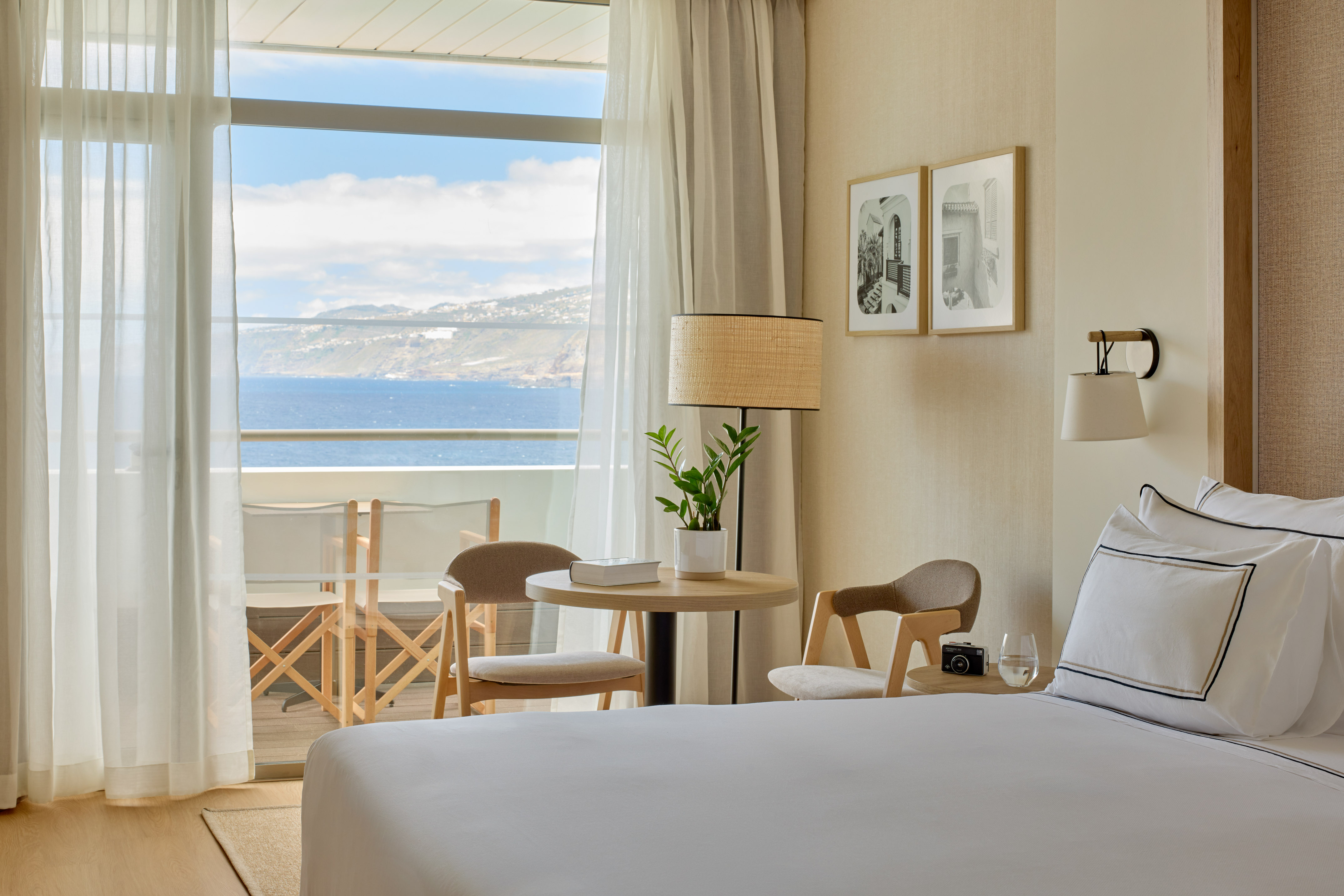 Hotel bedroom with ocean view balcony, white bed, and minimalist design.