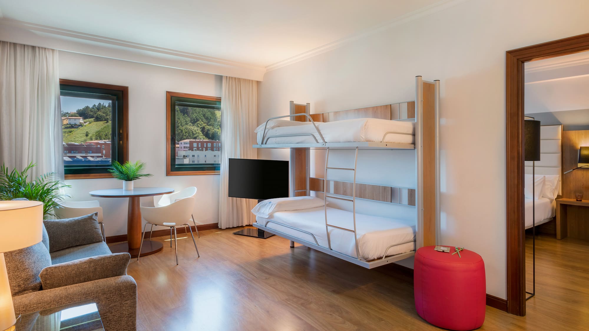 Hotel family room with modern bunk beds, sofa, dining area, and TV.