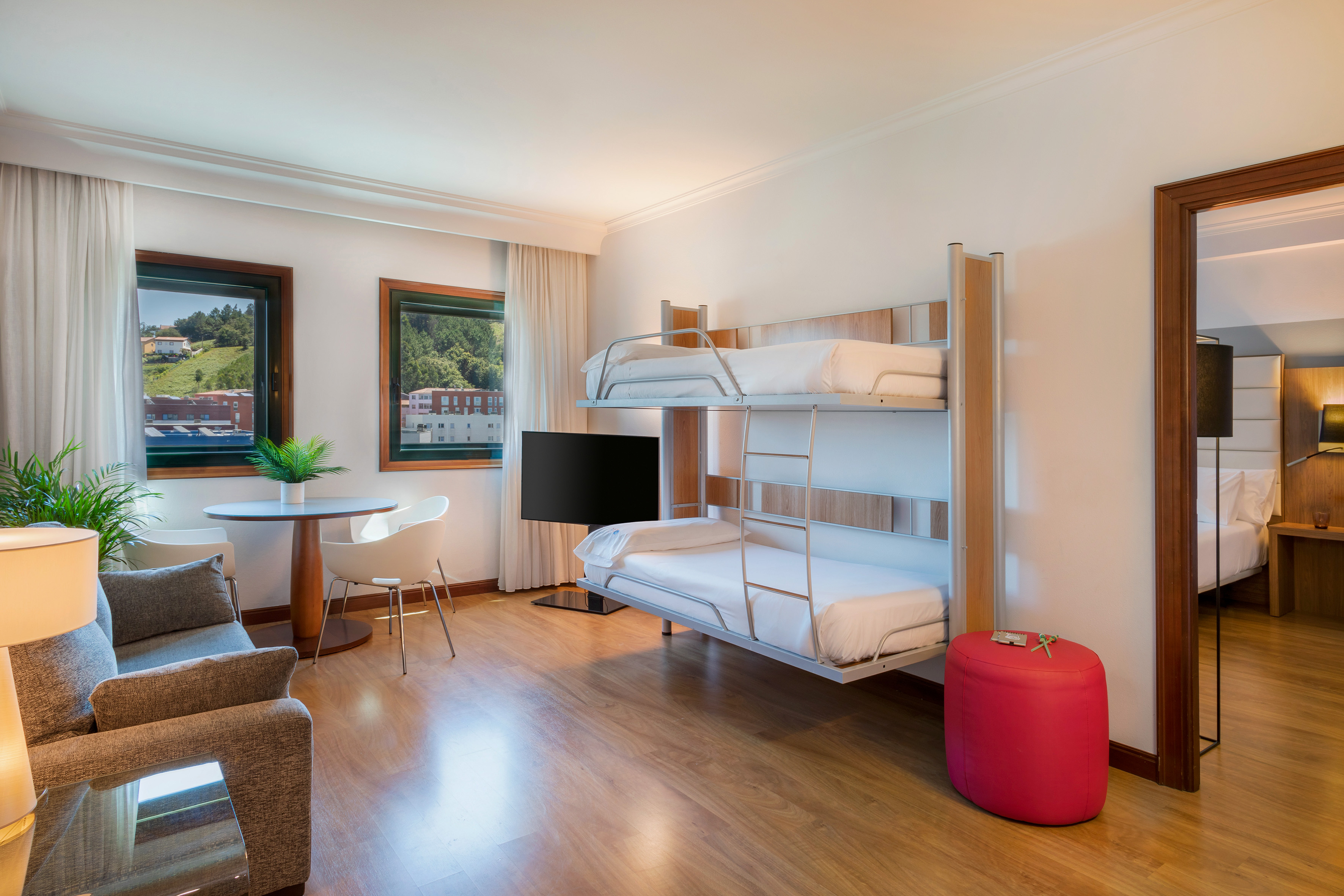 Hotel family room with modern bunk beds, sofa, dining area, and TV.