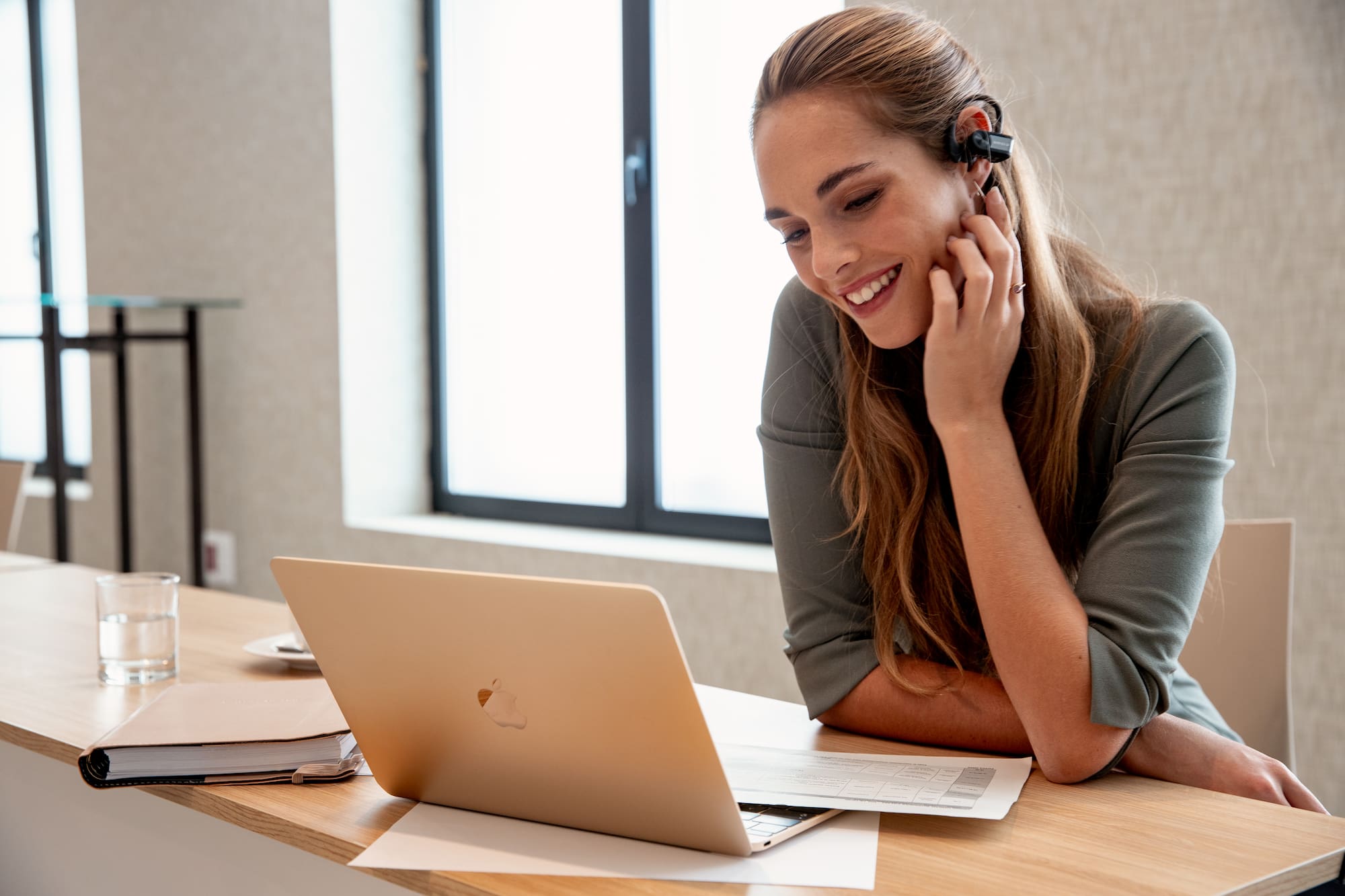 A woman with a headset gazes at a laptop.