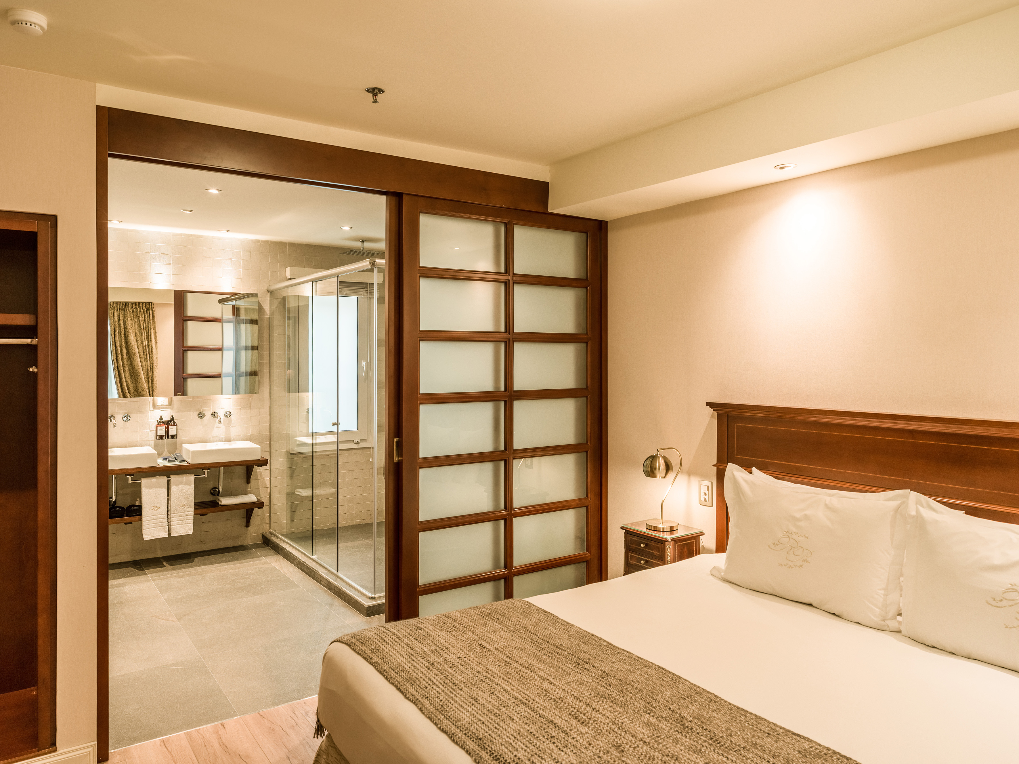 Modern hotel bedroom with bed, nightstand, and open-concept bathroom.