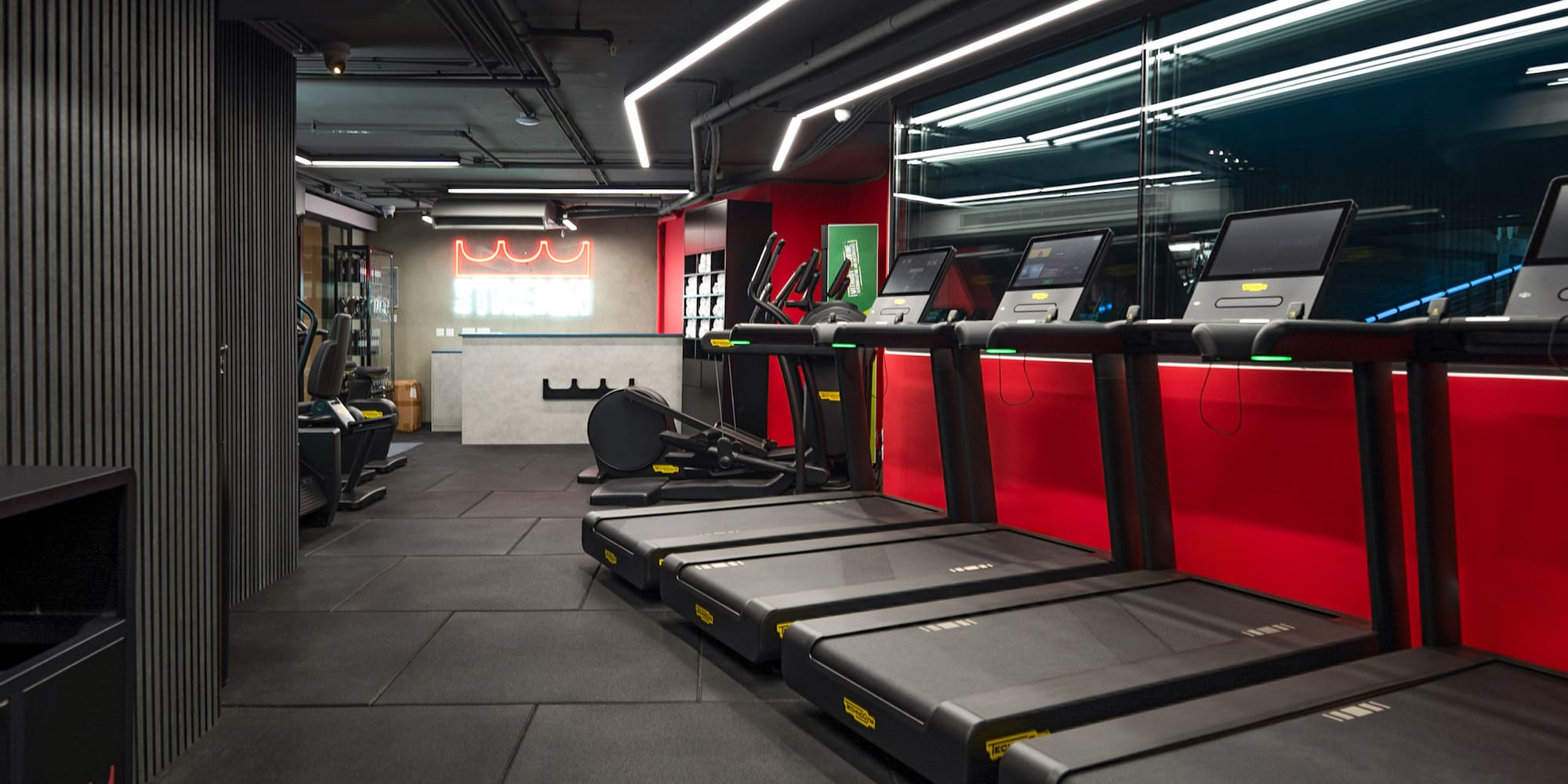 Modern gym with black treadmills, cardio machines, and 'STRENGTH' neon sign.