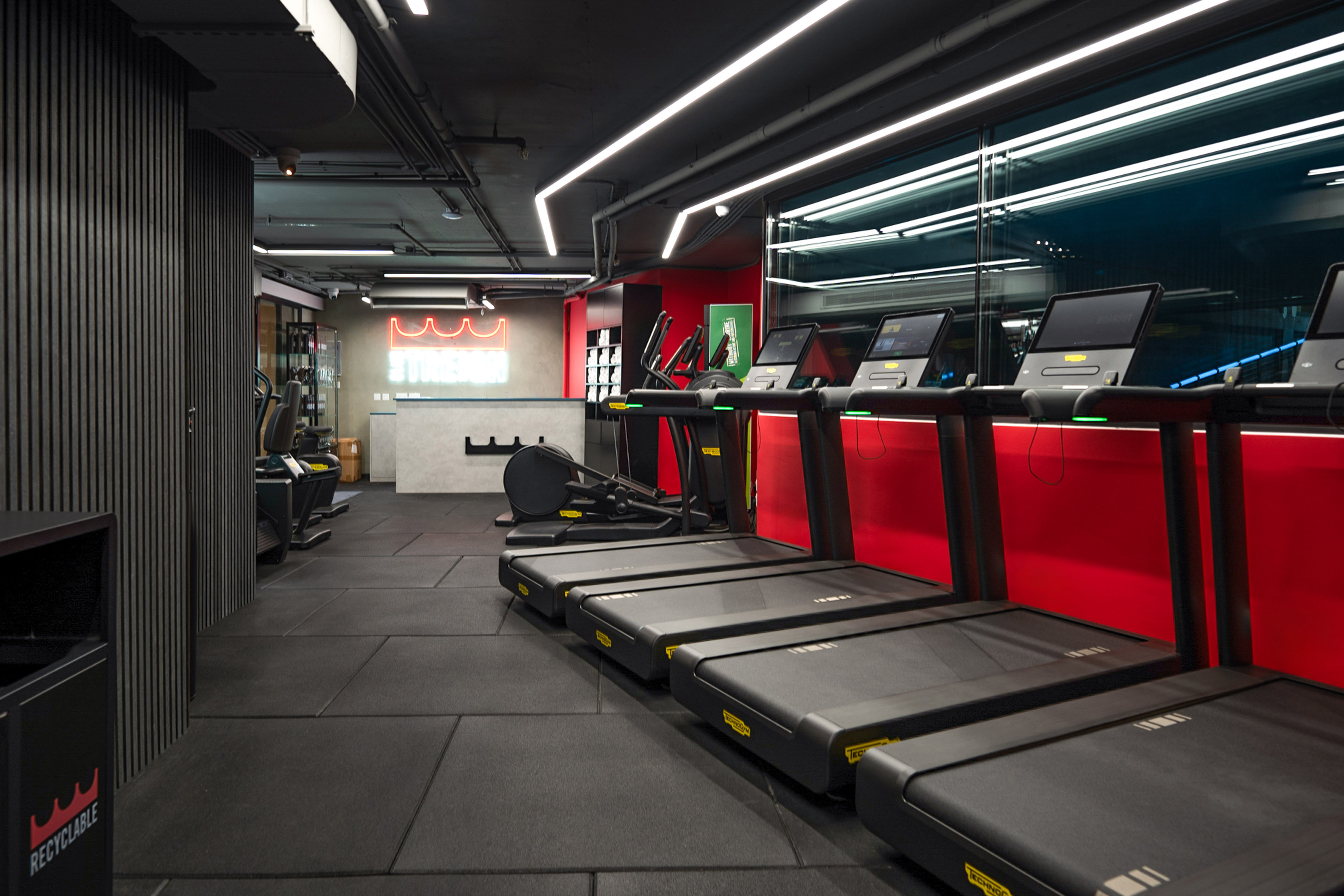 Modern gym with black treadmills, cardio machines, and 'STRENGTH' neon sign.