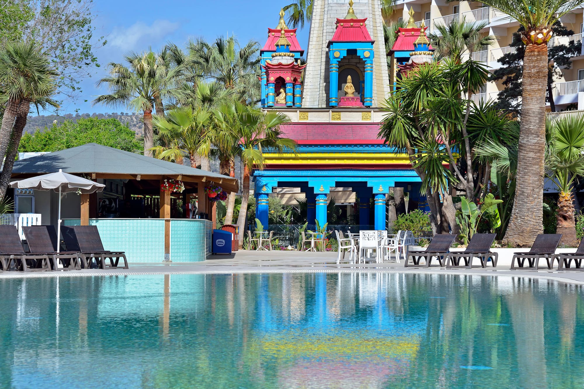 a pool with chairs and a building with a religious structure