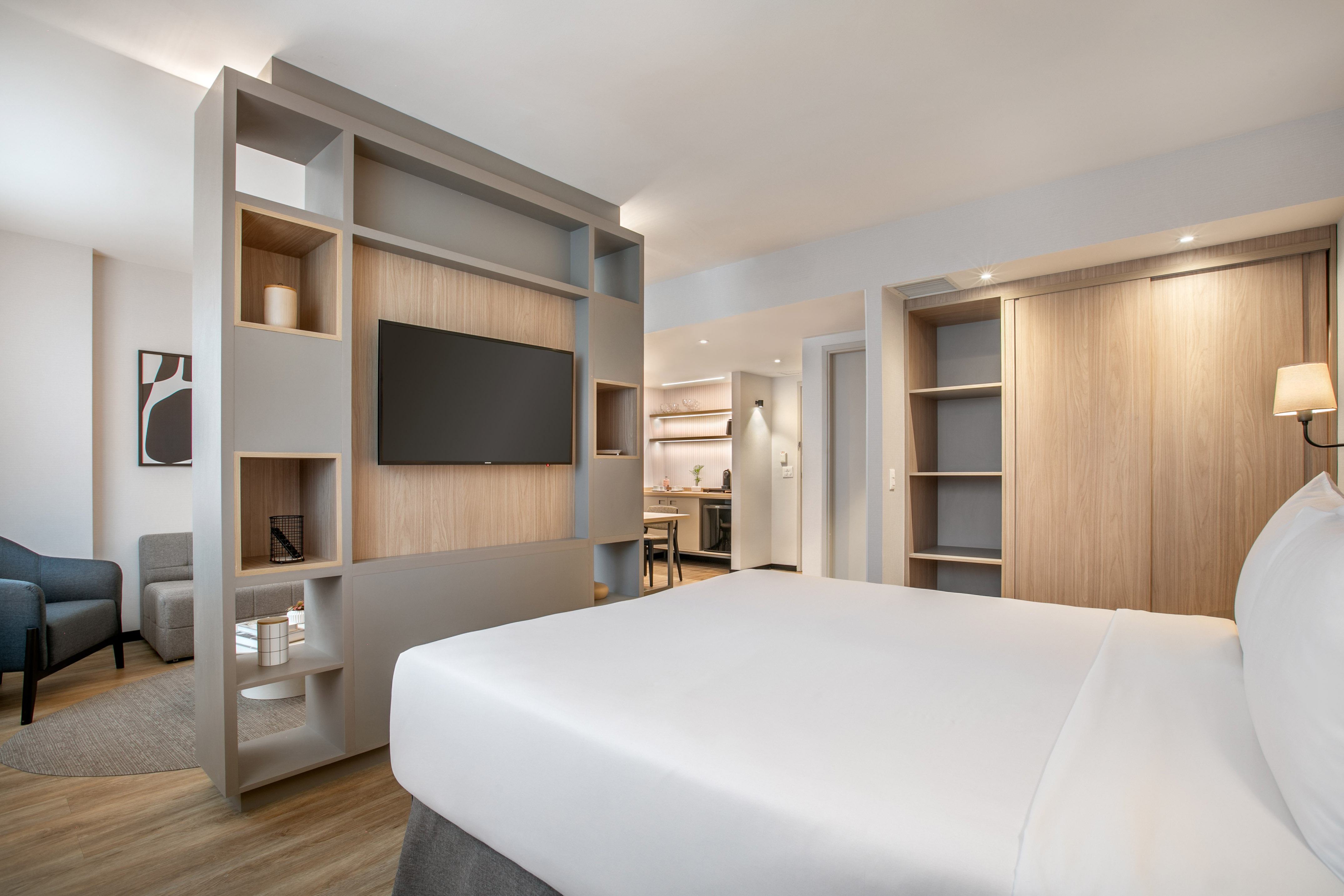 Modern hotel suite with bed, TV, living area, and kitchenette.