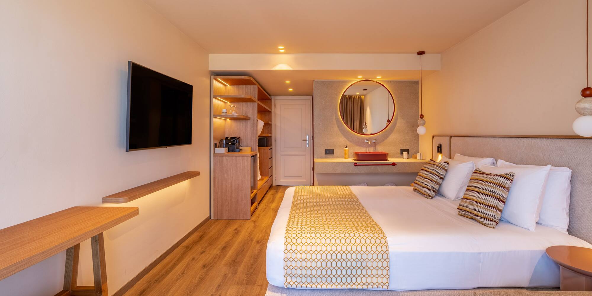 Modern hotel room with large bed, wall-mounted TV, and stylish red basin vanity.