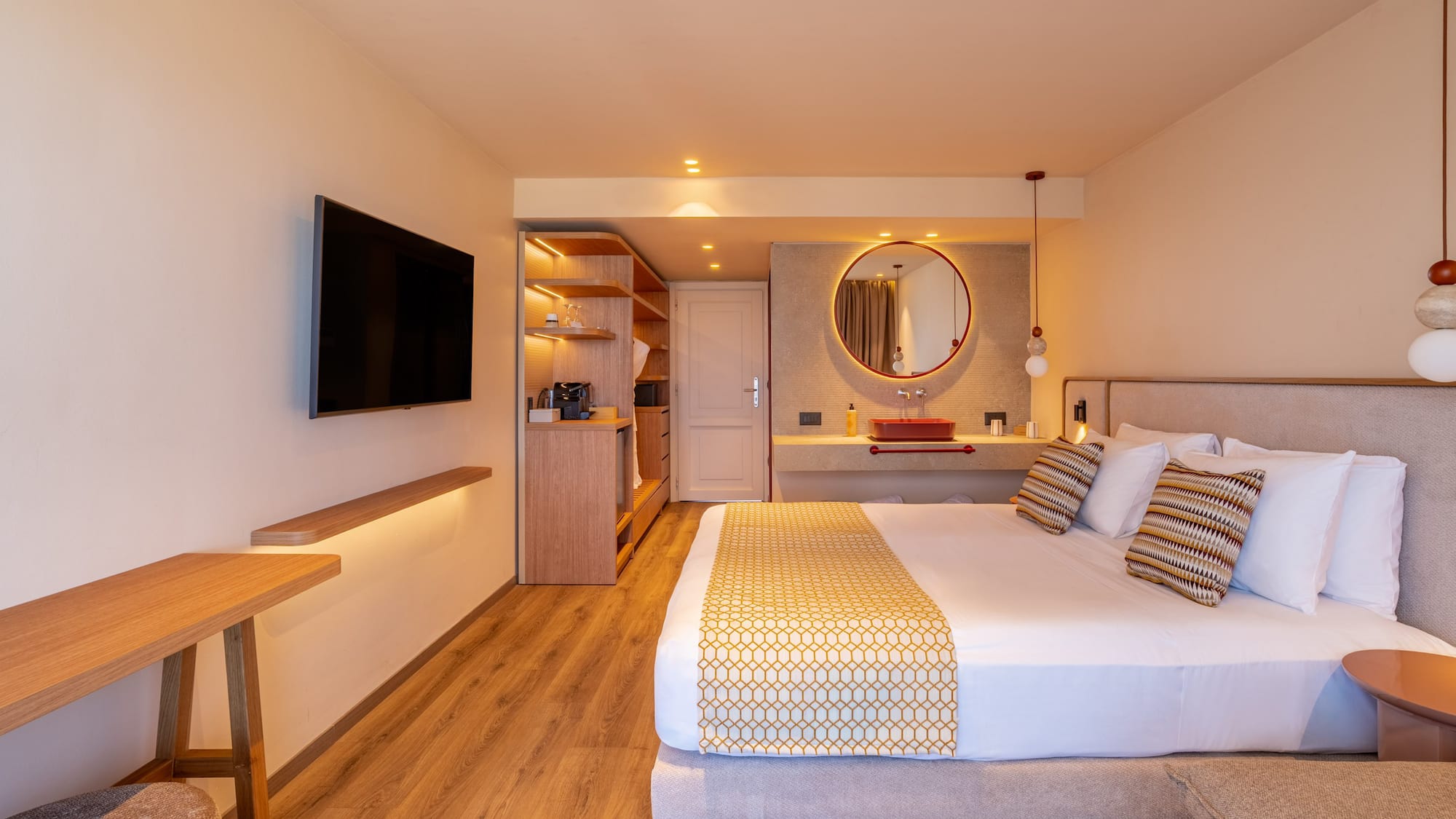Modern hotel room with large bed, wall-mounted TV, and stylish red basin vanity.