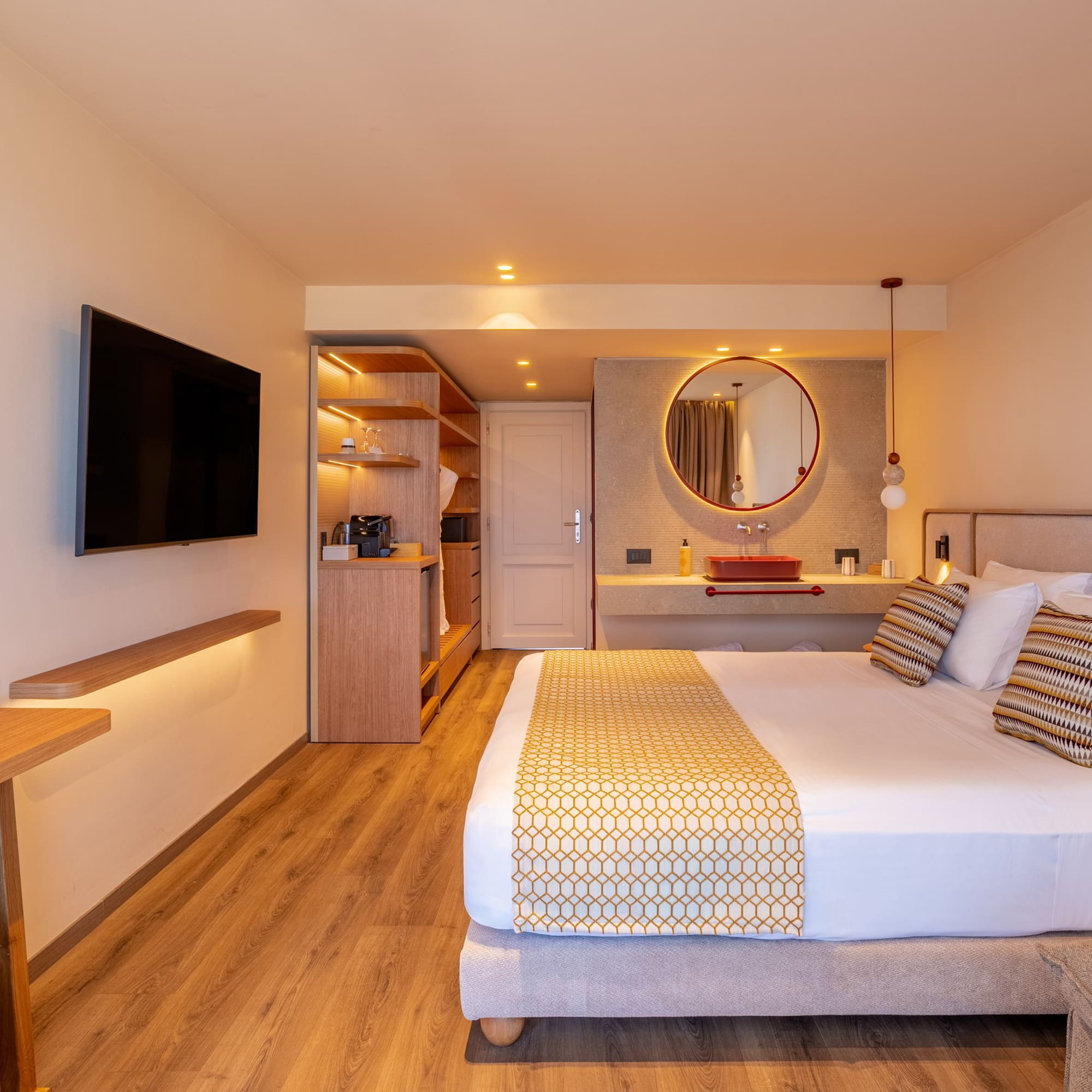 Modern hotel room with large bed, wall-mounted TV, and stylish red basin vanity.