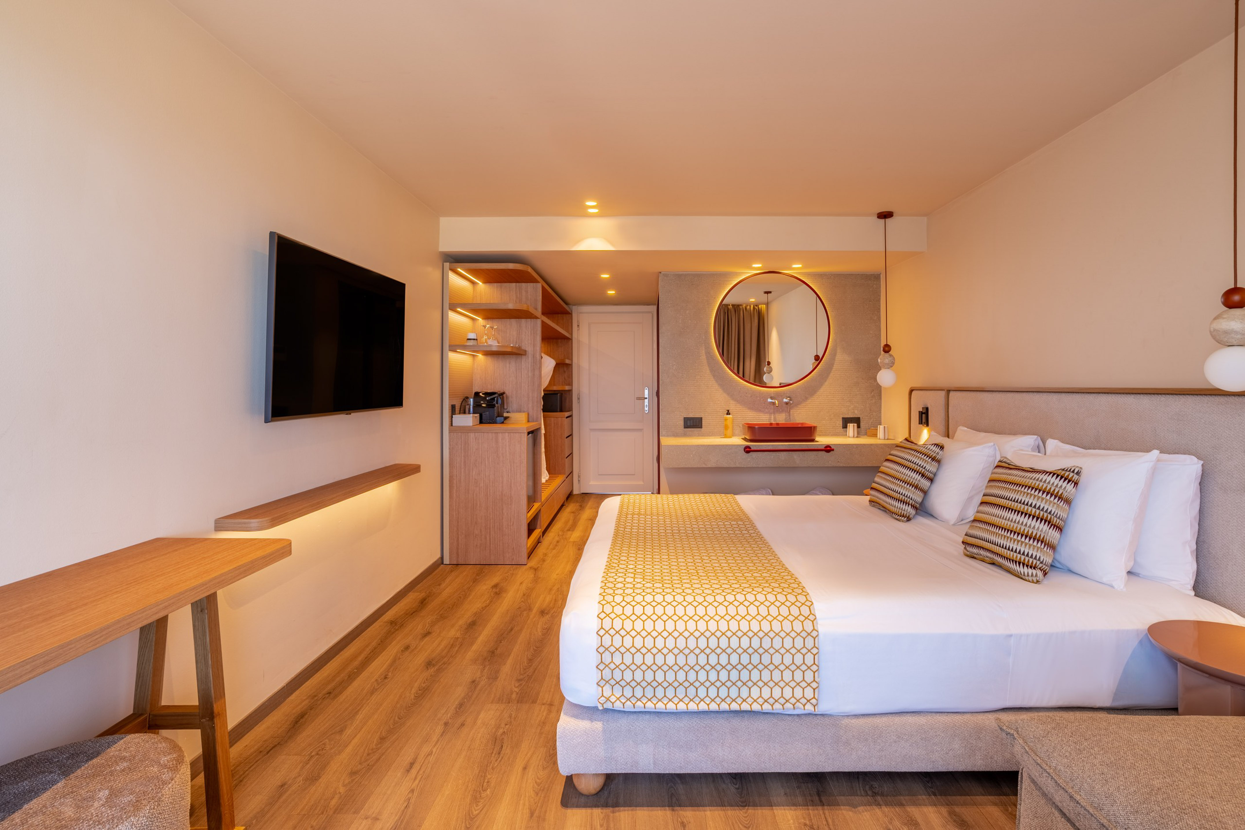 Modern hotel room with large bed, wall-mounted TV, and stylish red basin vanity.