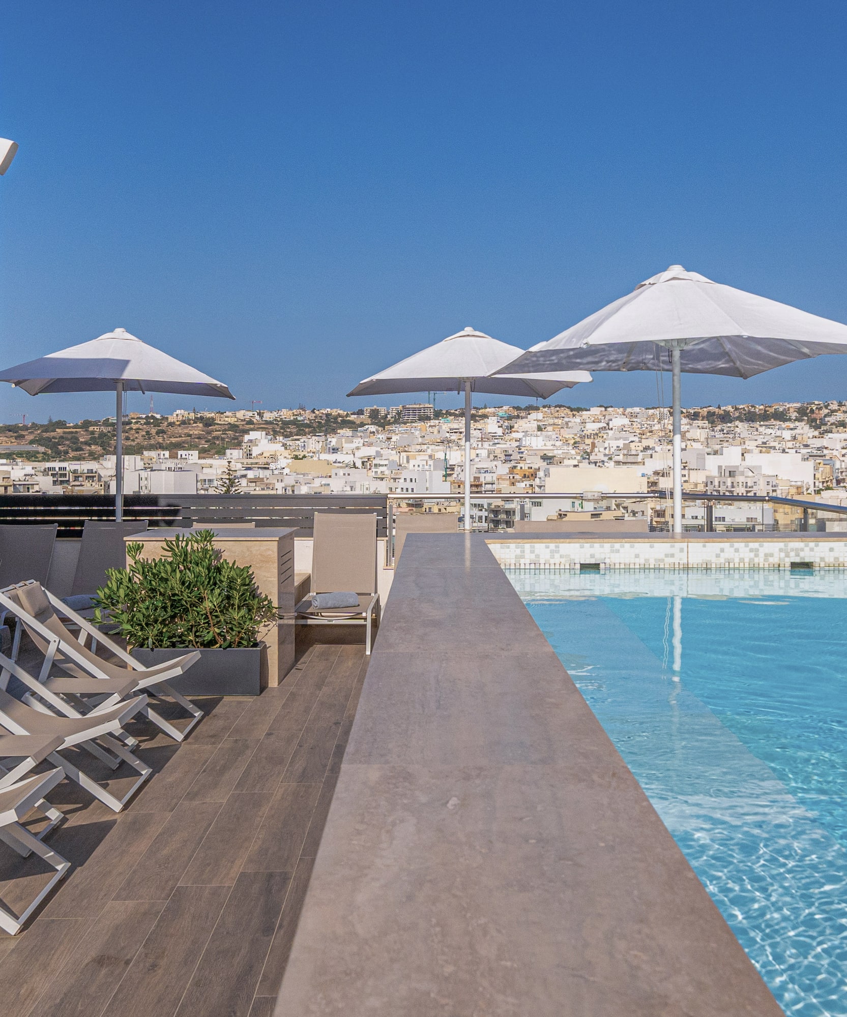 a pool with chairs and umbrellas on a rooftop