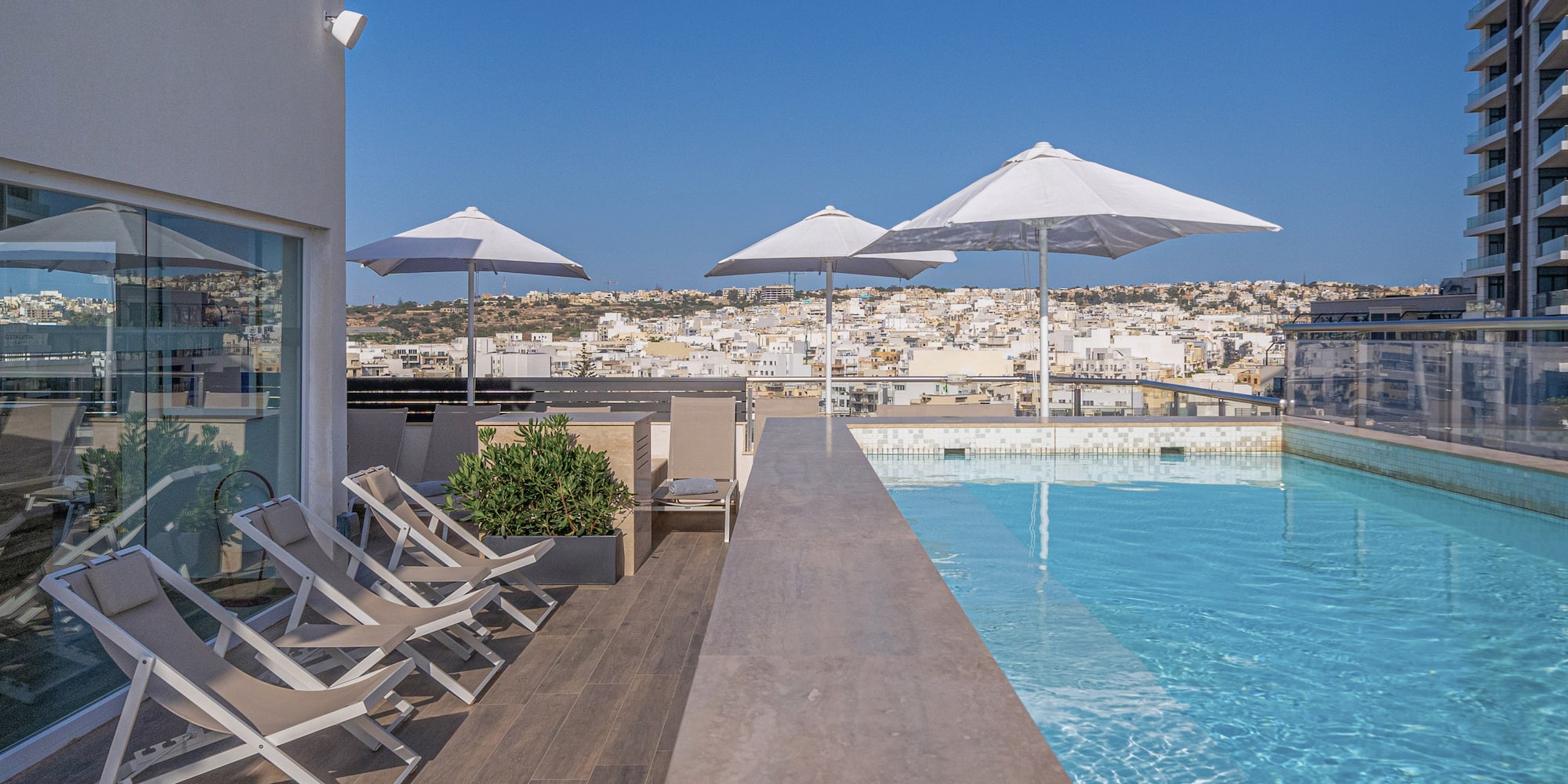a pool with chairs and umbrellas on a rooftop
