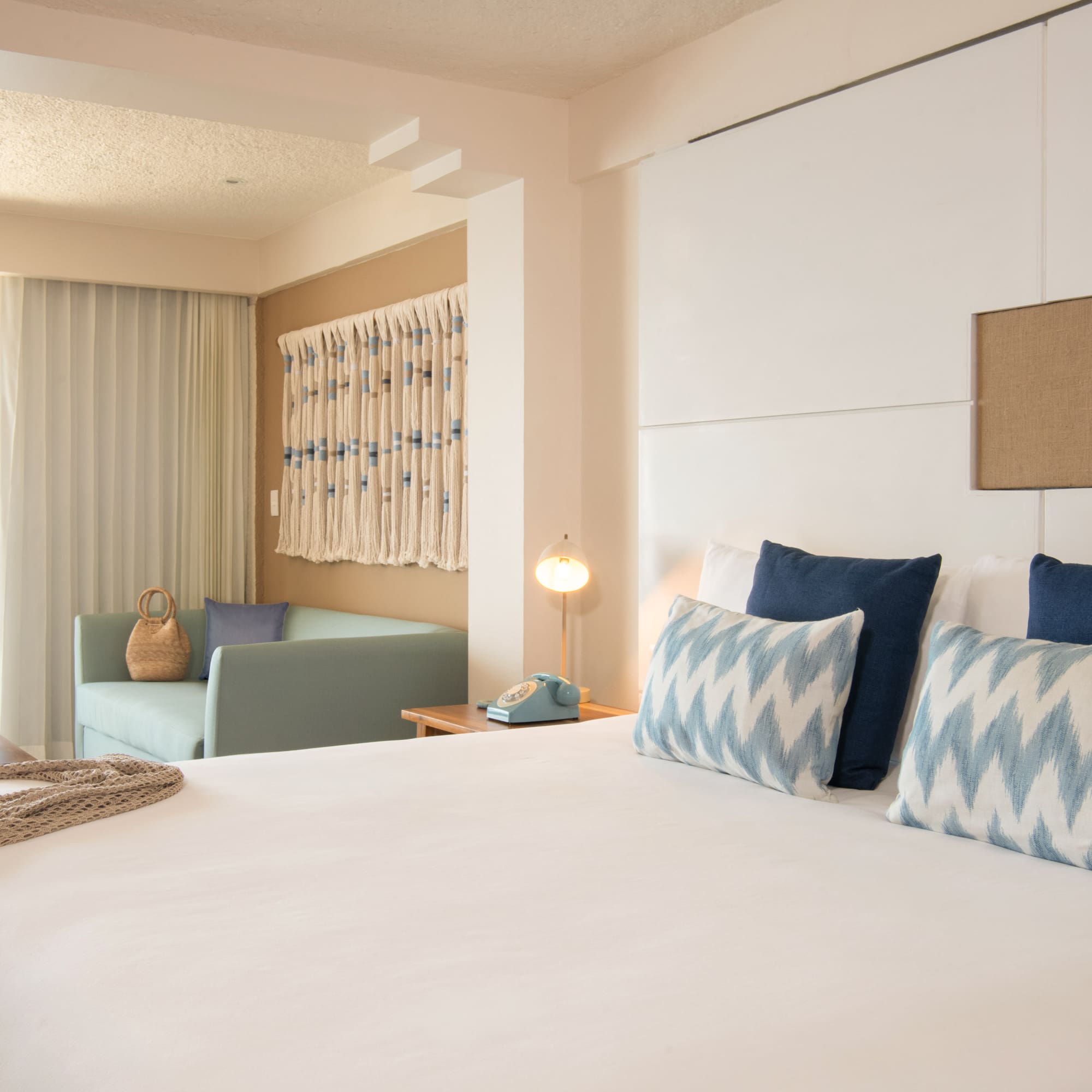 Hotel room with bed, blue pillows, sofa, and tropical palm garden view.