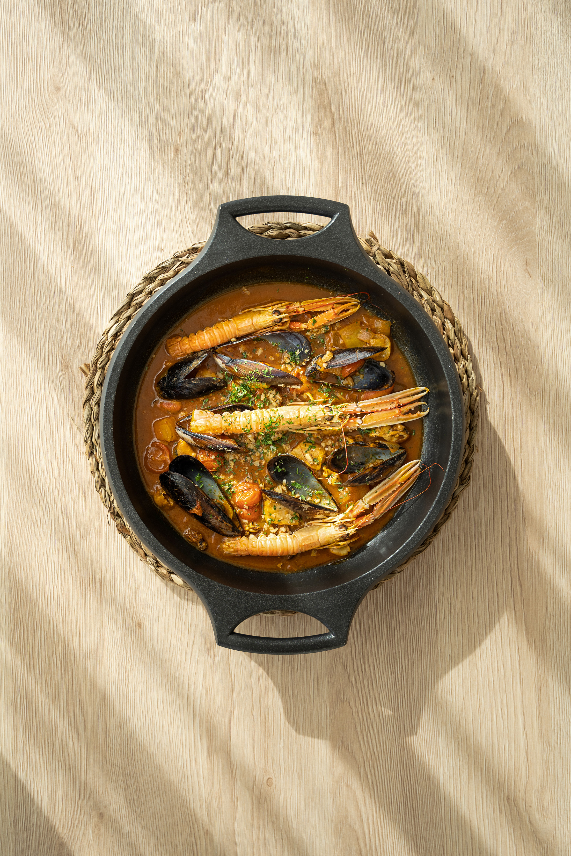 Mediterranean seafood stew with mussels, langoustines, herbs in a black pan.