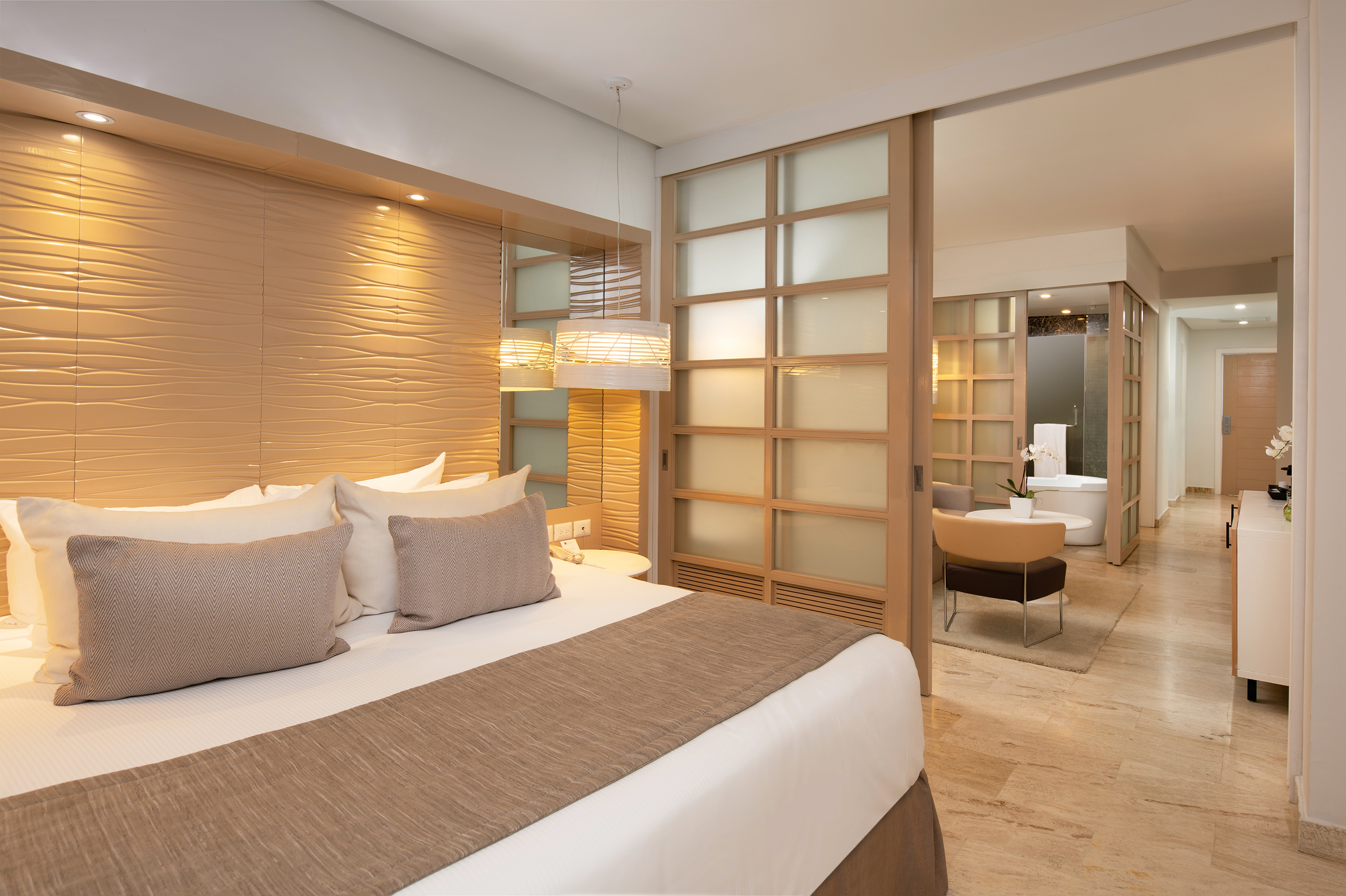 Modern hotel suite with king bed, textured headboard, and open bathroom.