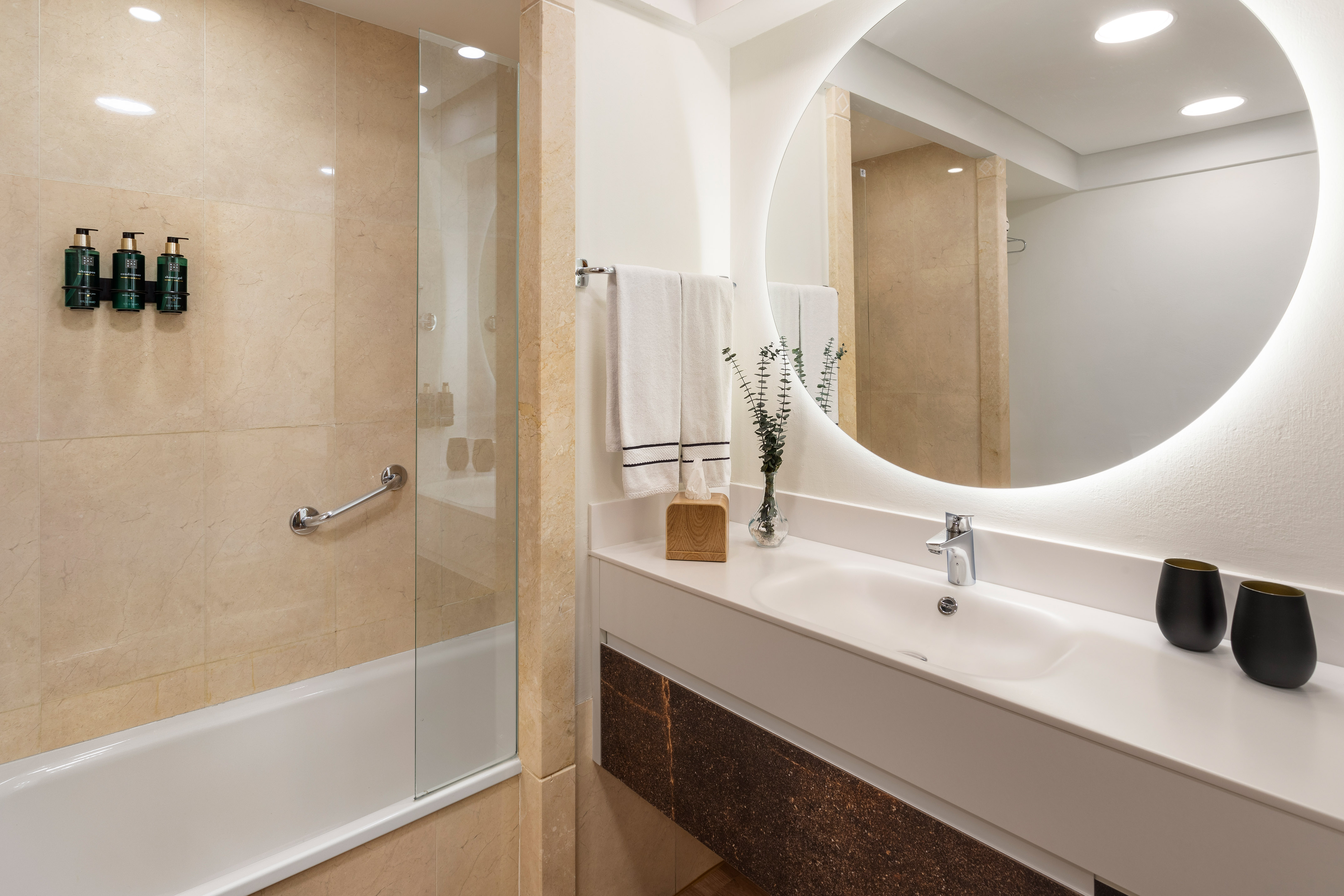 Modern hotel bathroom with bathtub, vanity, backlit mirror, and amenities.