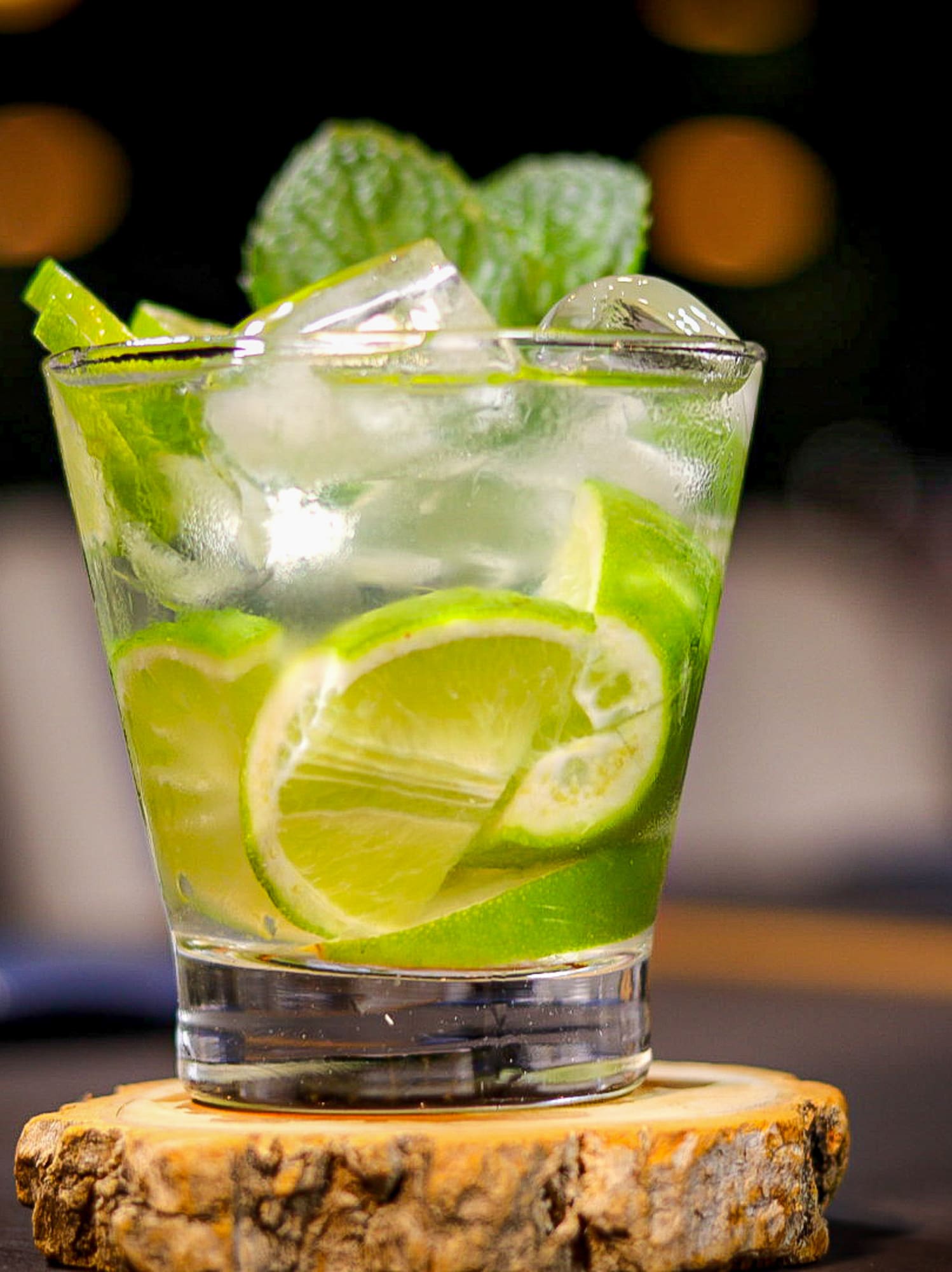 a glass with limes and mint leaves on a wood slice