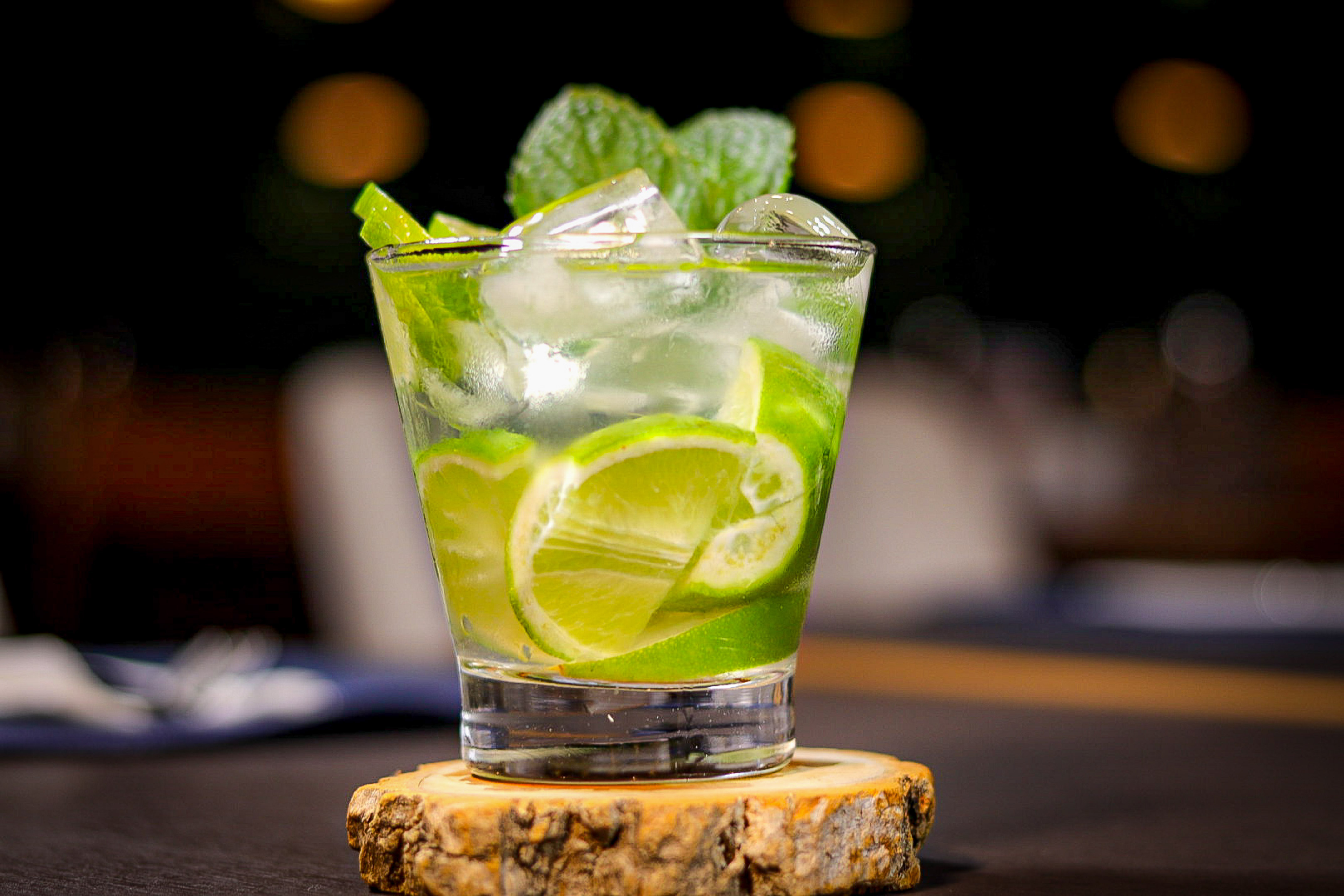a glass with limes and mint leaves on a wood slice