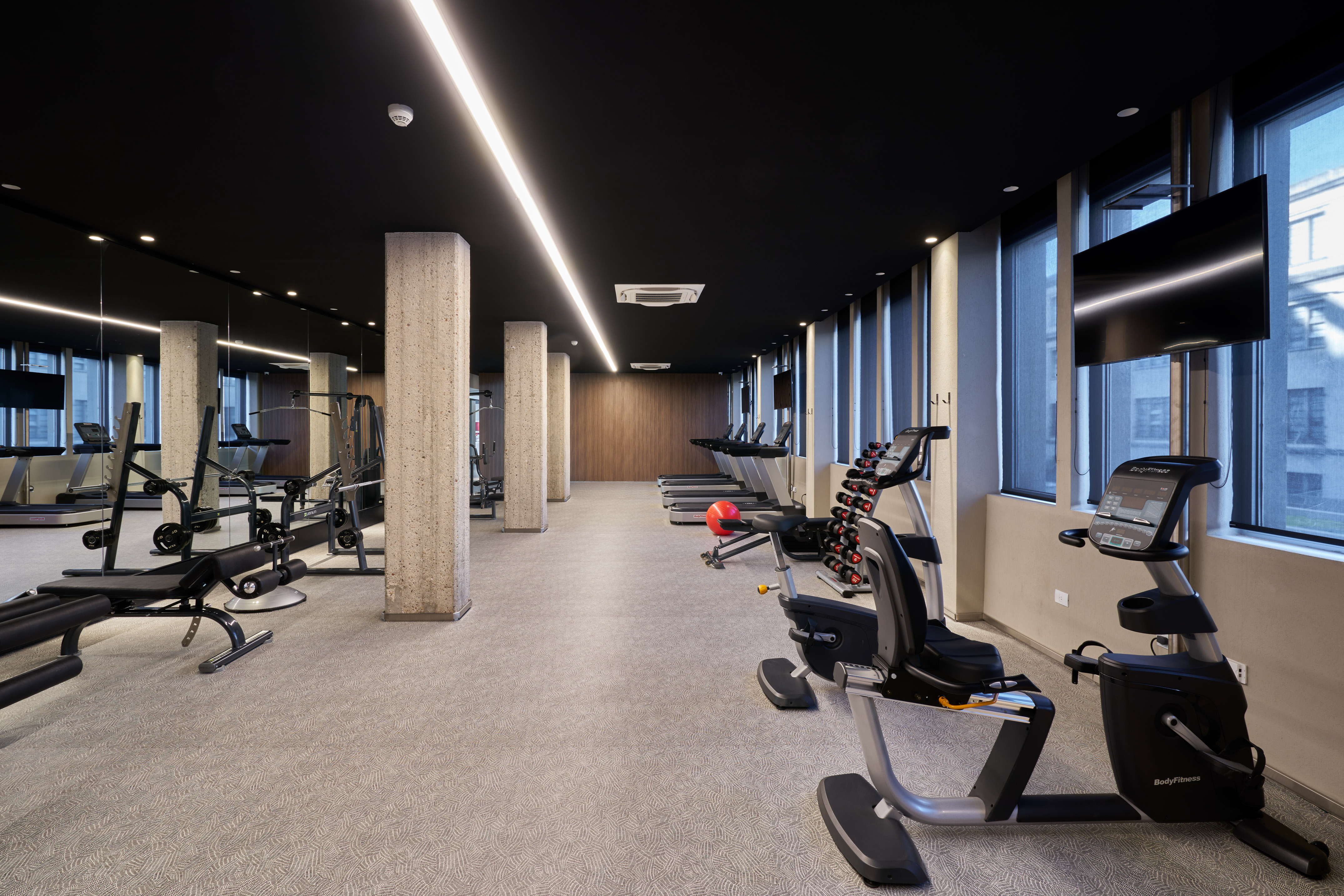 Modern fitness center with treadmills, exercise bikes, weights, and concrete pillars.