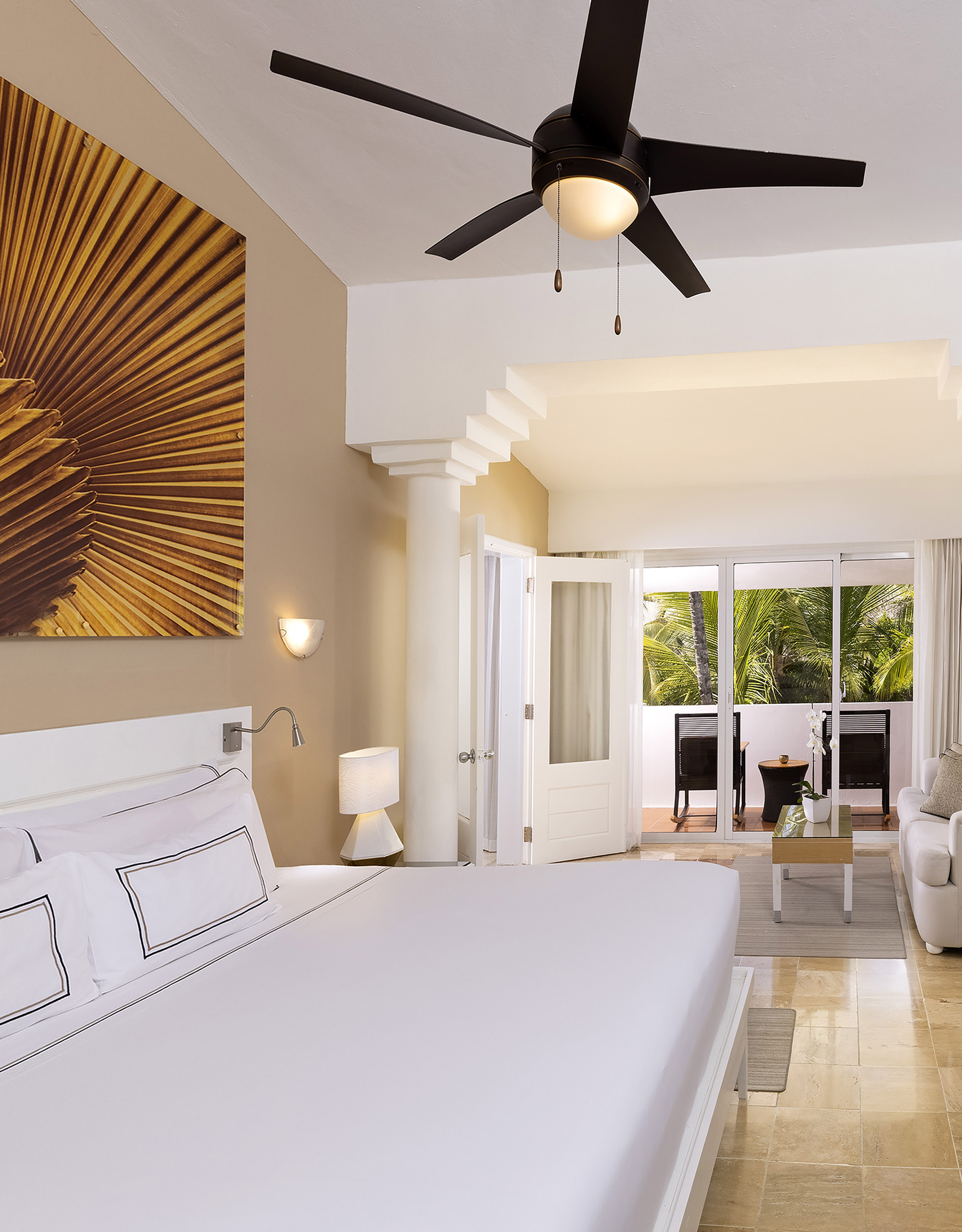 Spacious hotel room with king bed, ceiling fan, and tropical balcony view.