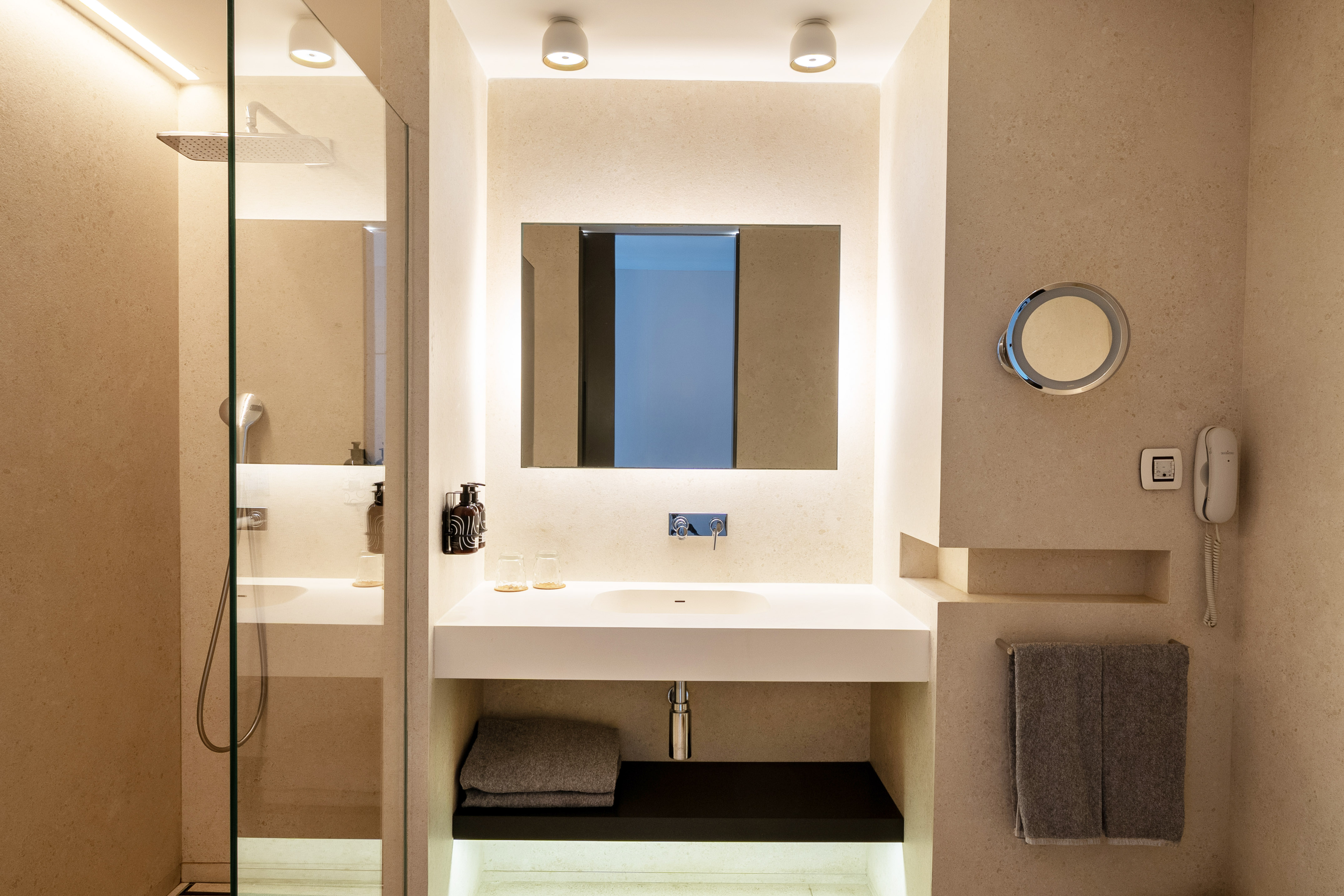 Contemporary beige bathroom with backlit mirror, white sink vanity, and glass shower.