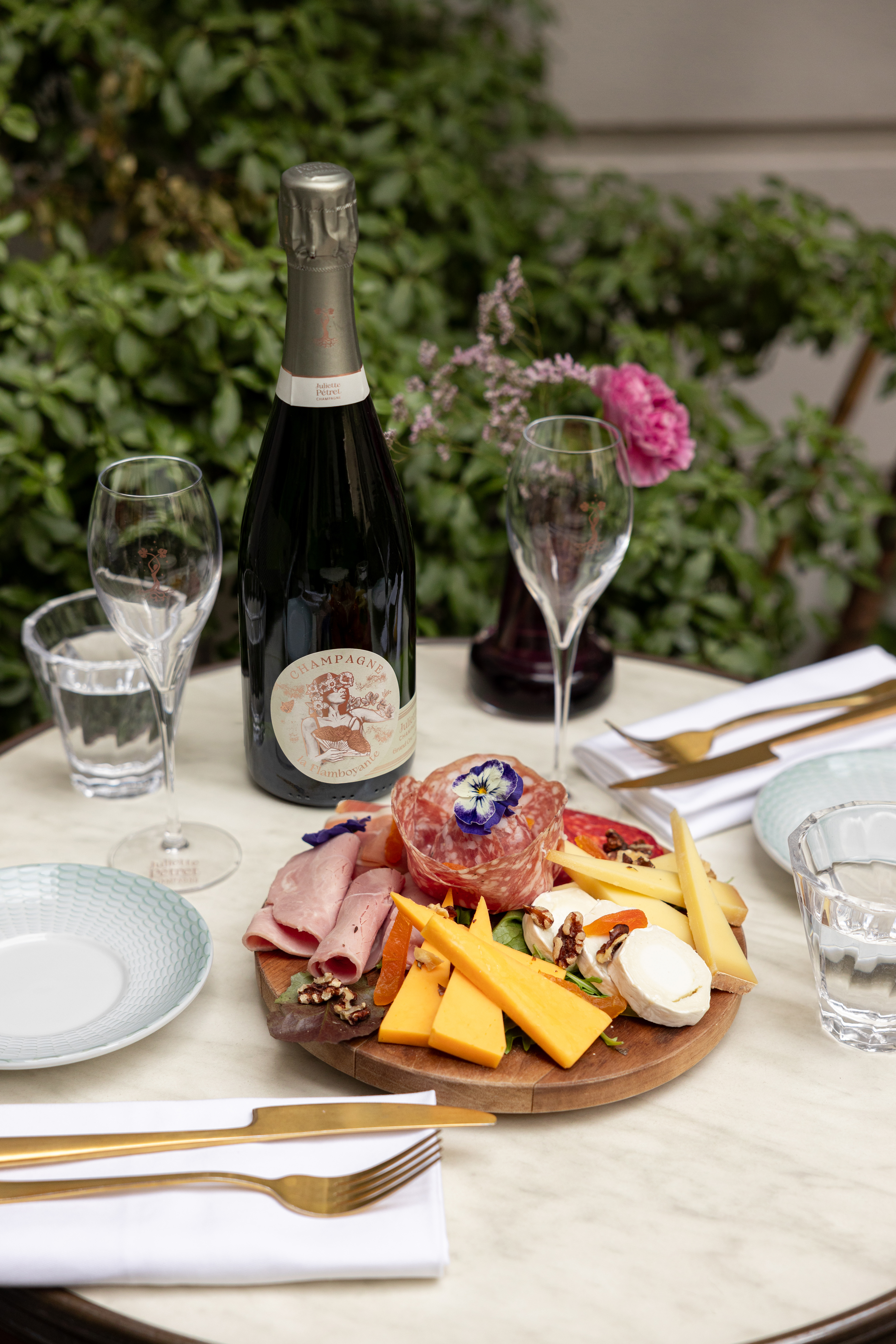 Champagne bottle, charcuterie and cheese board on an outdoor table.