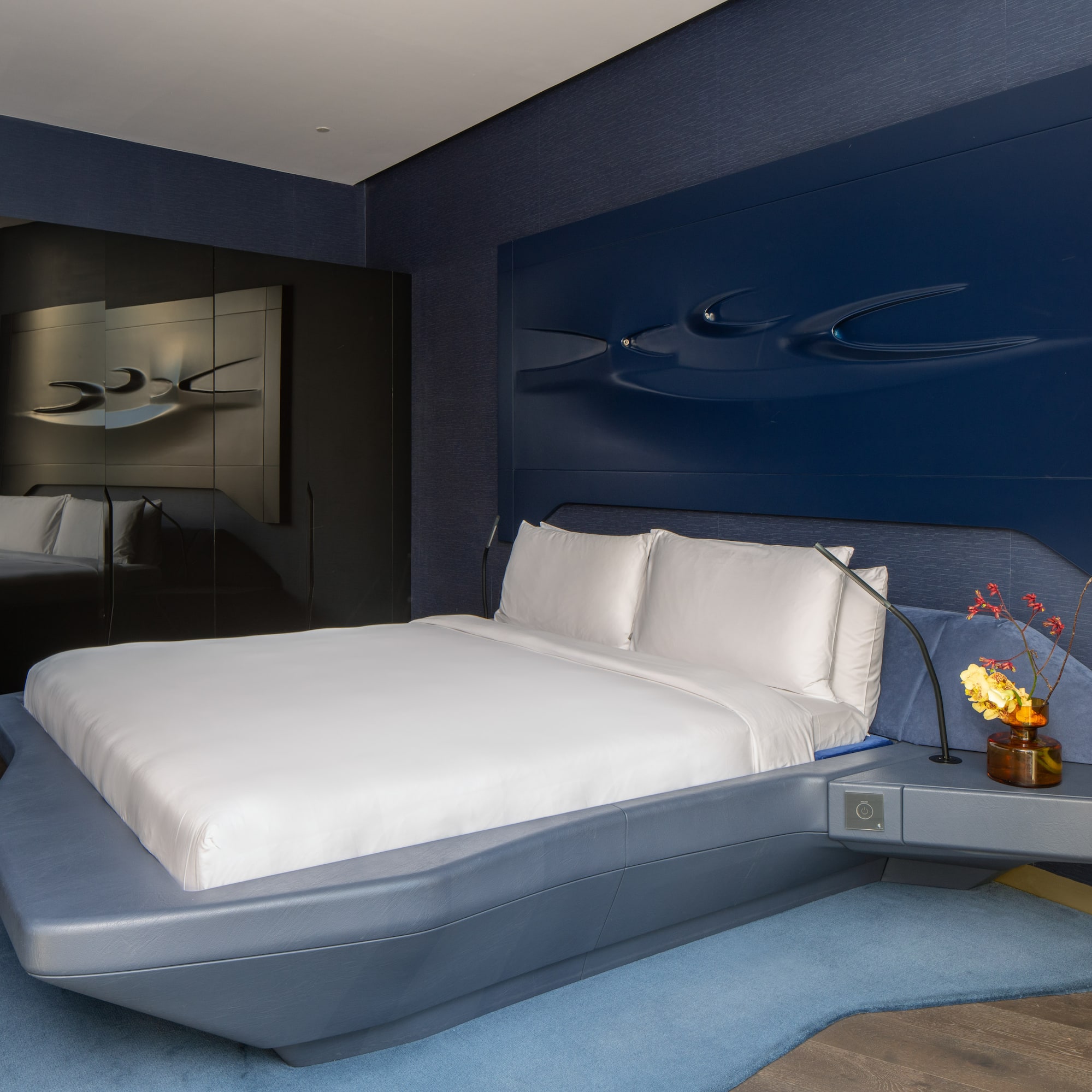 Modern blue hotel bedroom with sculptural headboard, floating bed.