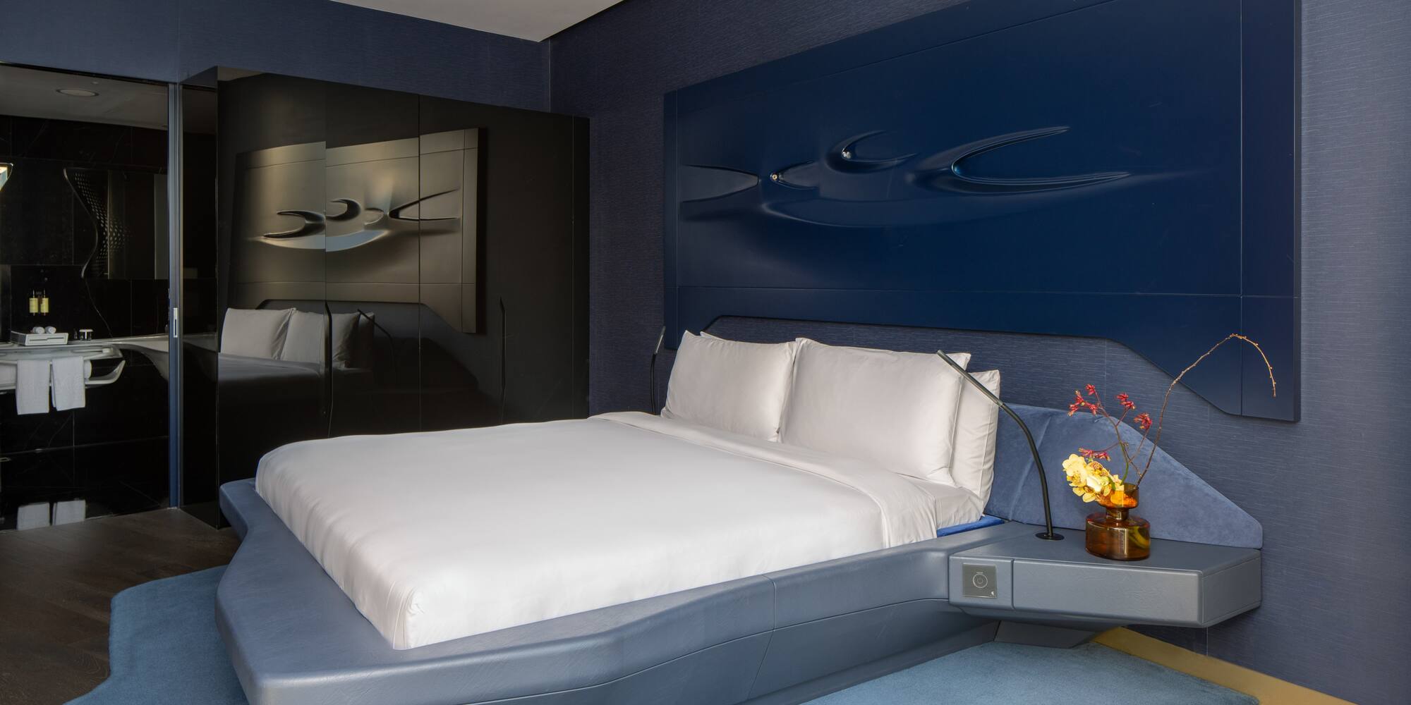 Modern blue hotel bedroom with sculptural headboard, floating bed.