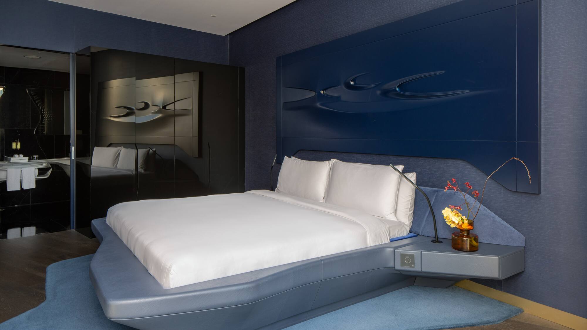 Modern blue hotel bedroom with sculptural headboard, floating bed.