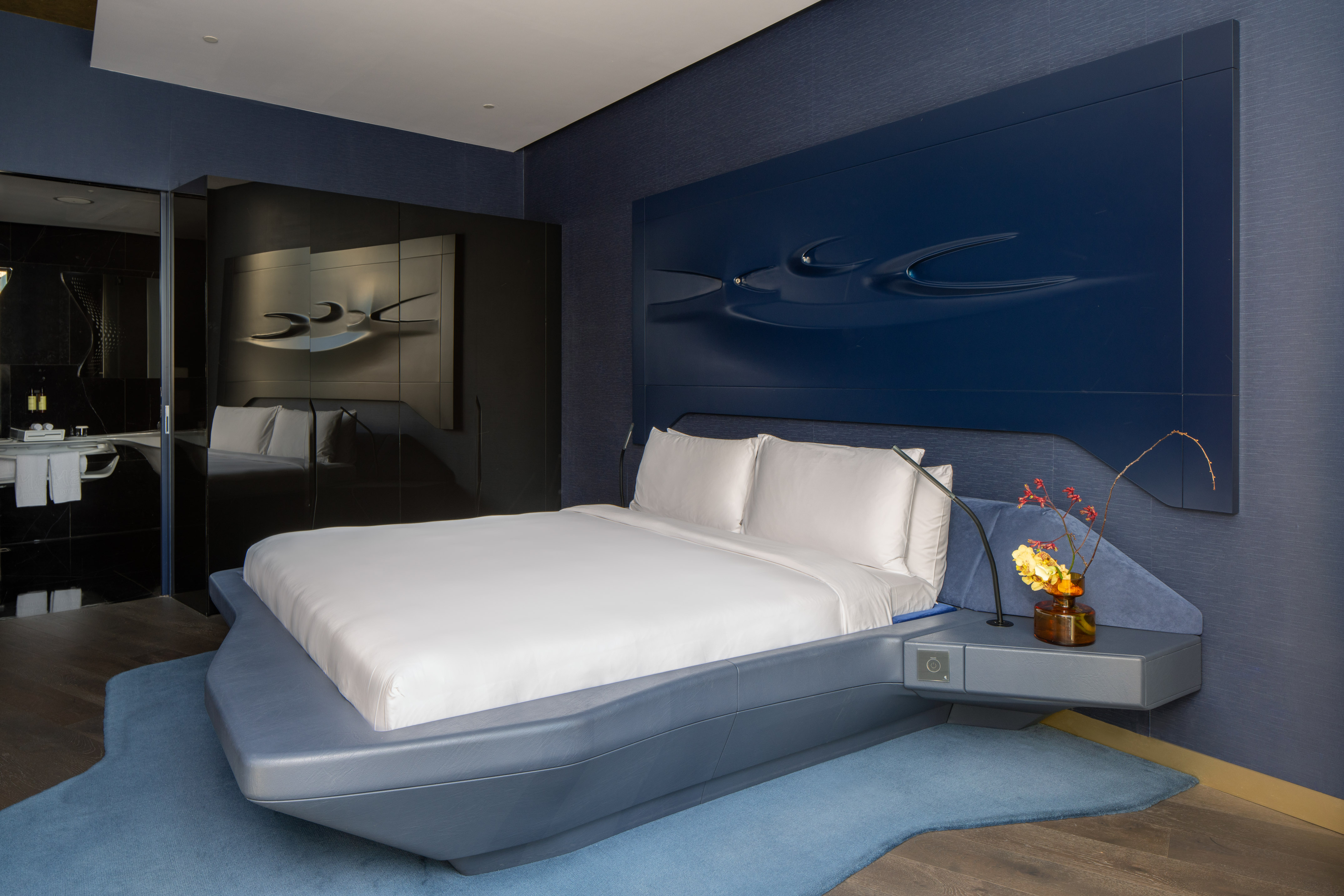 Modern blue hotel bedroom with sculptural headboard, floating bed.