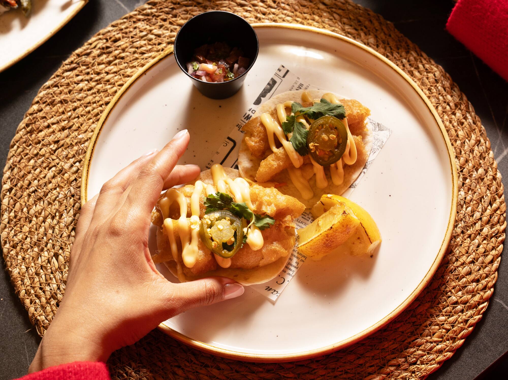 Person grabbing fish tacos with jalapeños, salsa, wine, and patatas bravas.