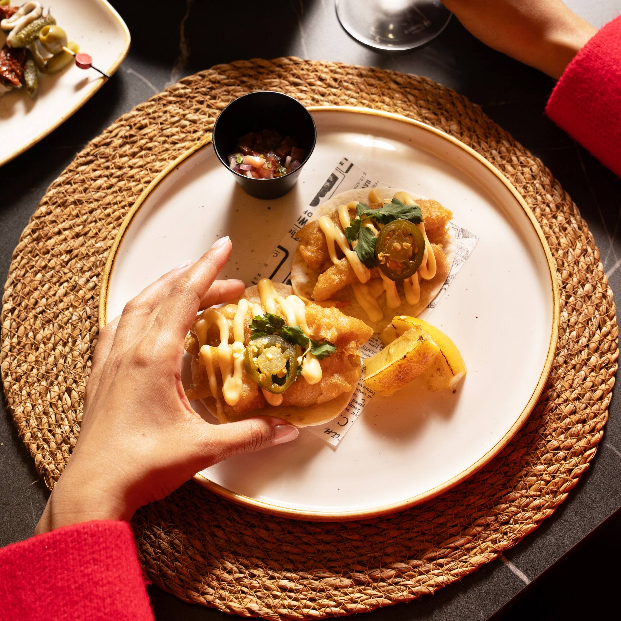 Person grabbing fish tacos with jalapeños, salsa, wine, and patatas bravas.