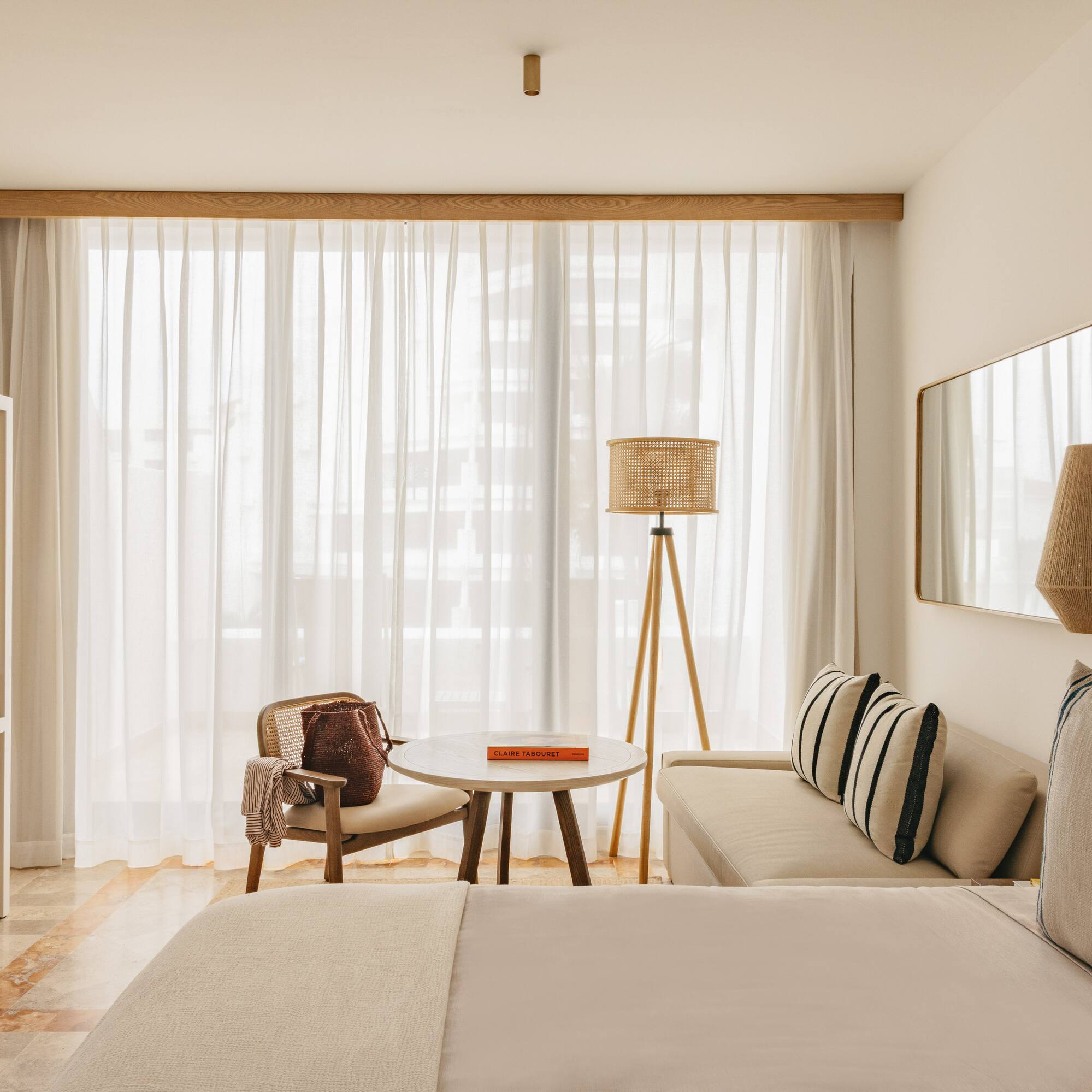 Minimalist hotel room with light wood, rattan decor, and bright window.