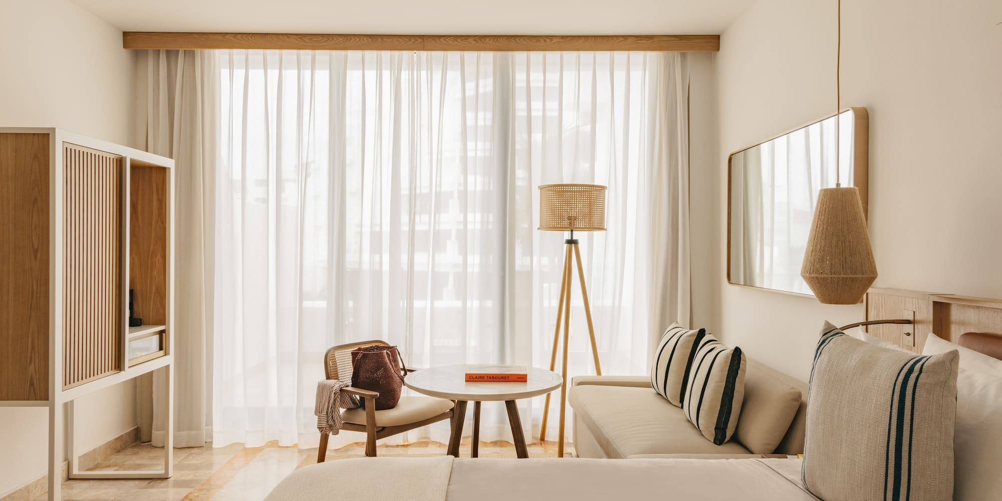 Minimalist hotel room with light wood, rattan decor, and bright window.