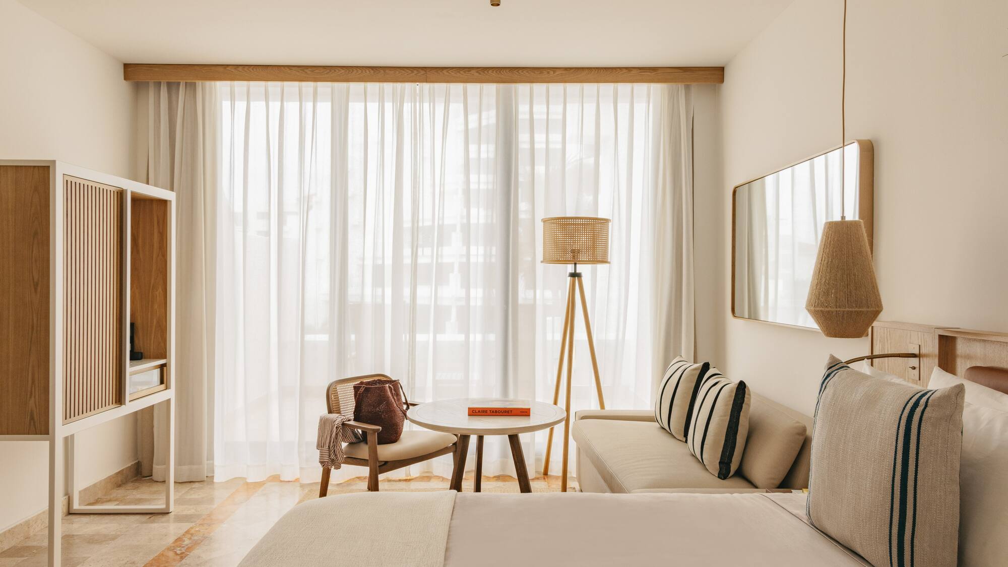 Minimalist hotel room with light wood, rattan decor, and bright window.