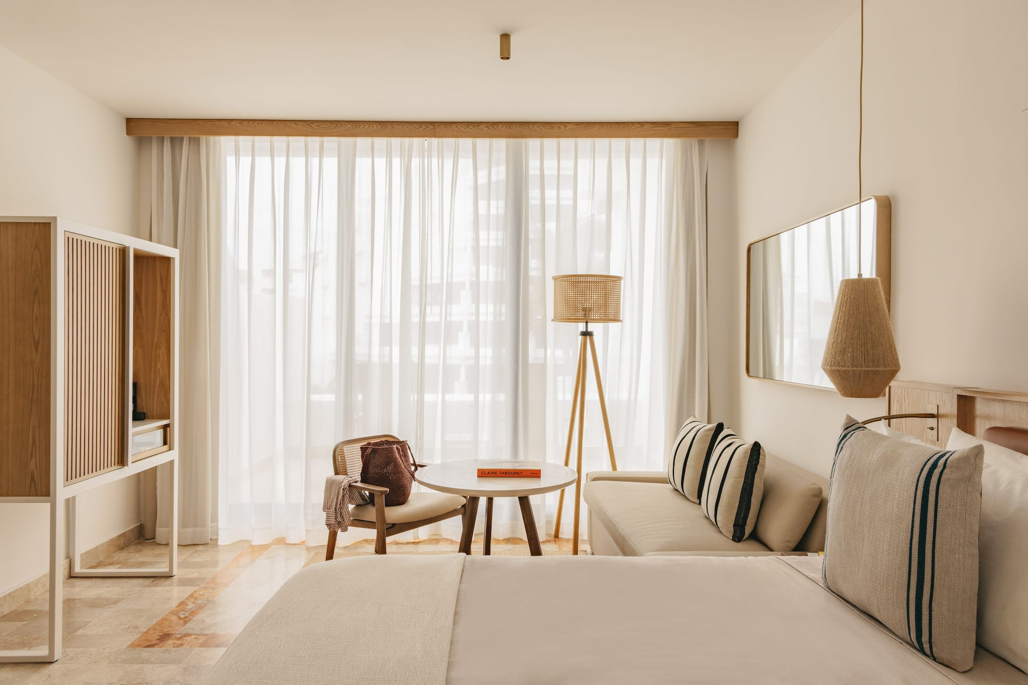 Minimalist hotel room with light wood, rattan decor, and bright window.