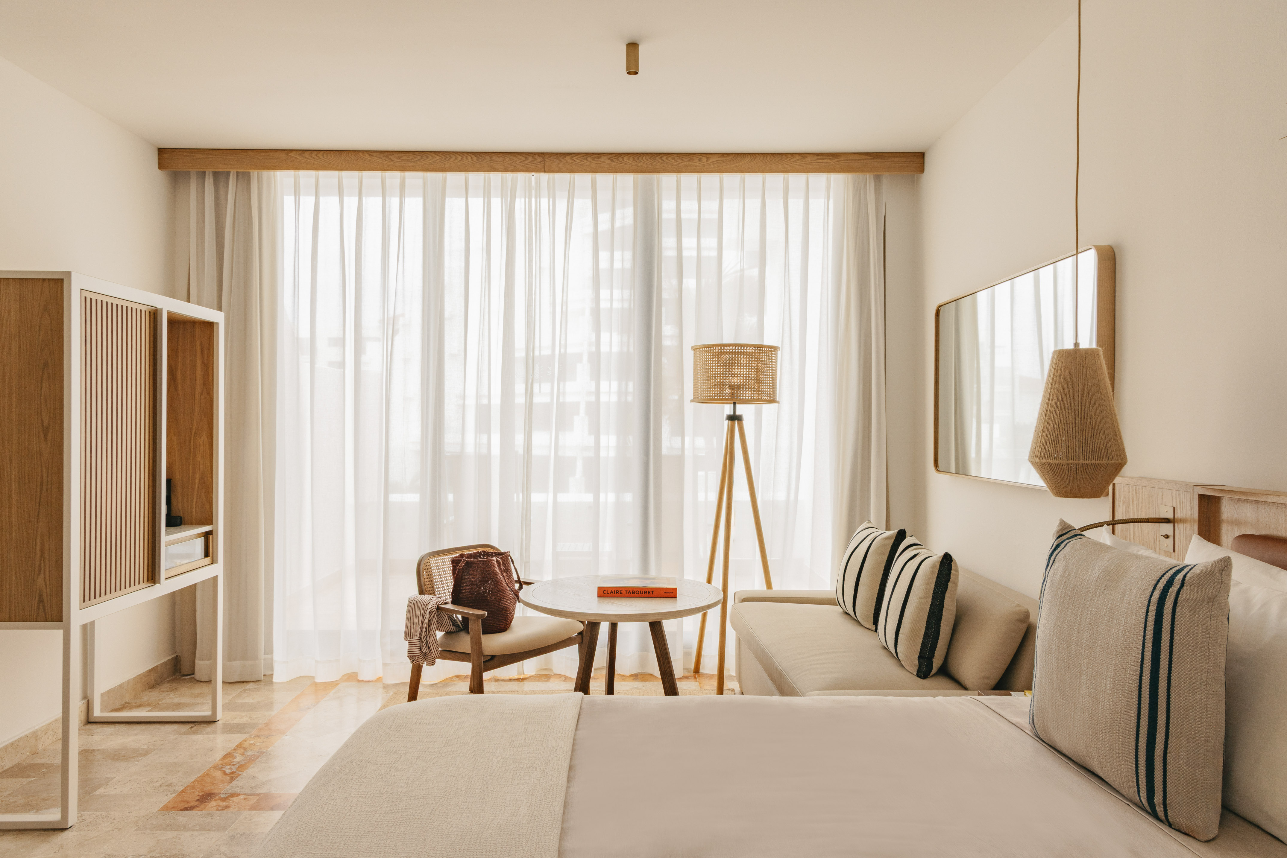Chic neutral bedroom with bed, lounge, rattan accents, and bright window.