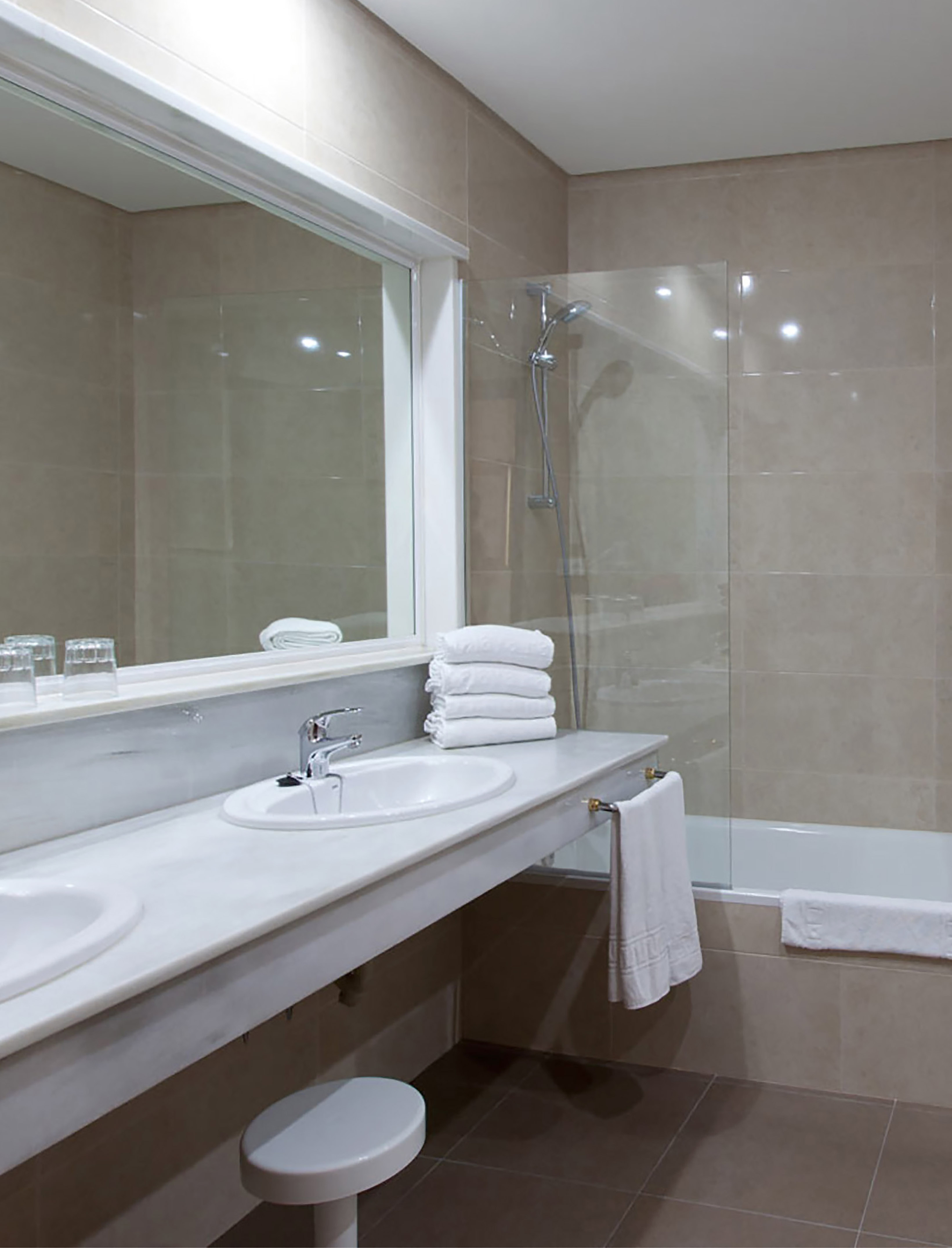 Bathroom with double sinks, large mirror, shower, tub, beige tiles, white towels.