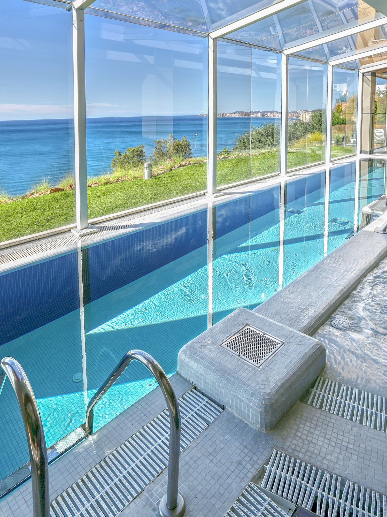Glass-enclosed indoor pool and hot tub with panoramic ocean view.