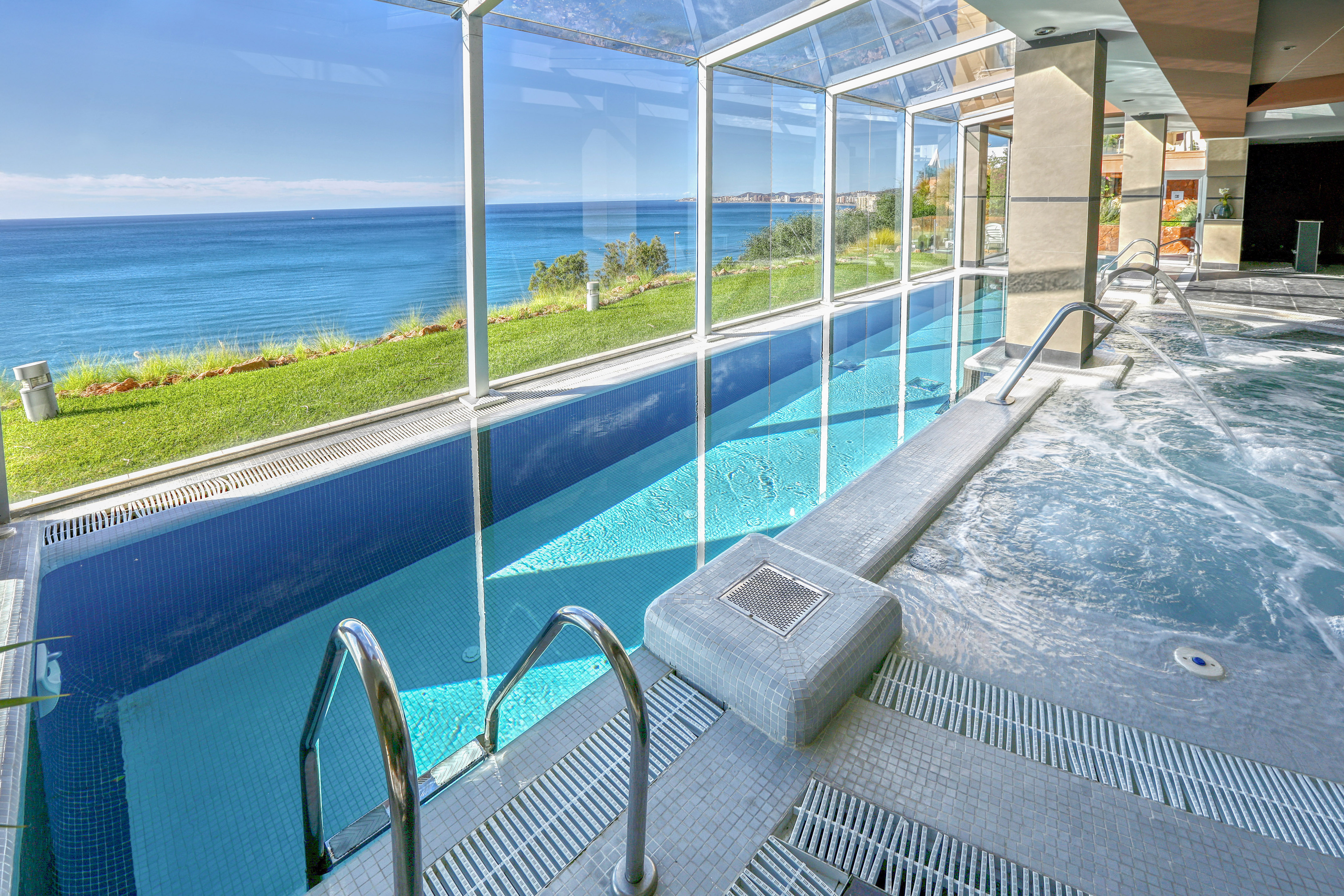 Glass-enclosed indoor pool and hot tub with panoramic ocean view.