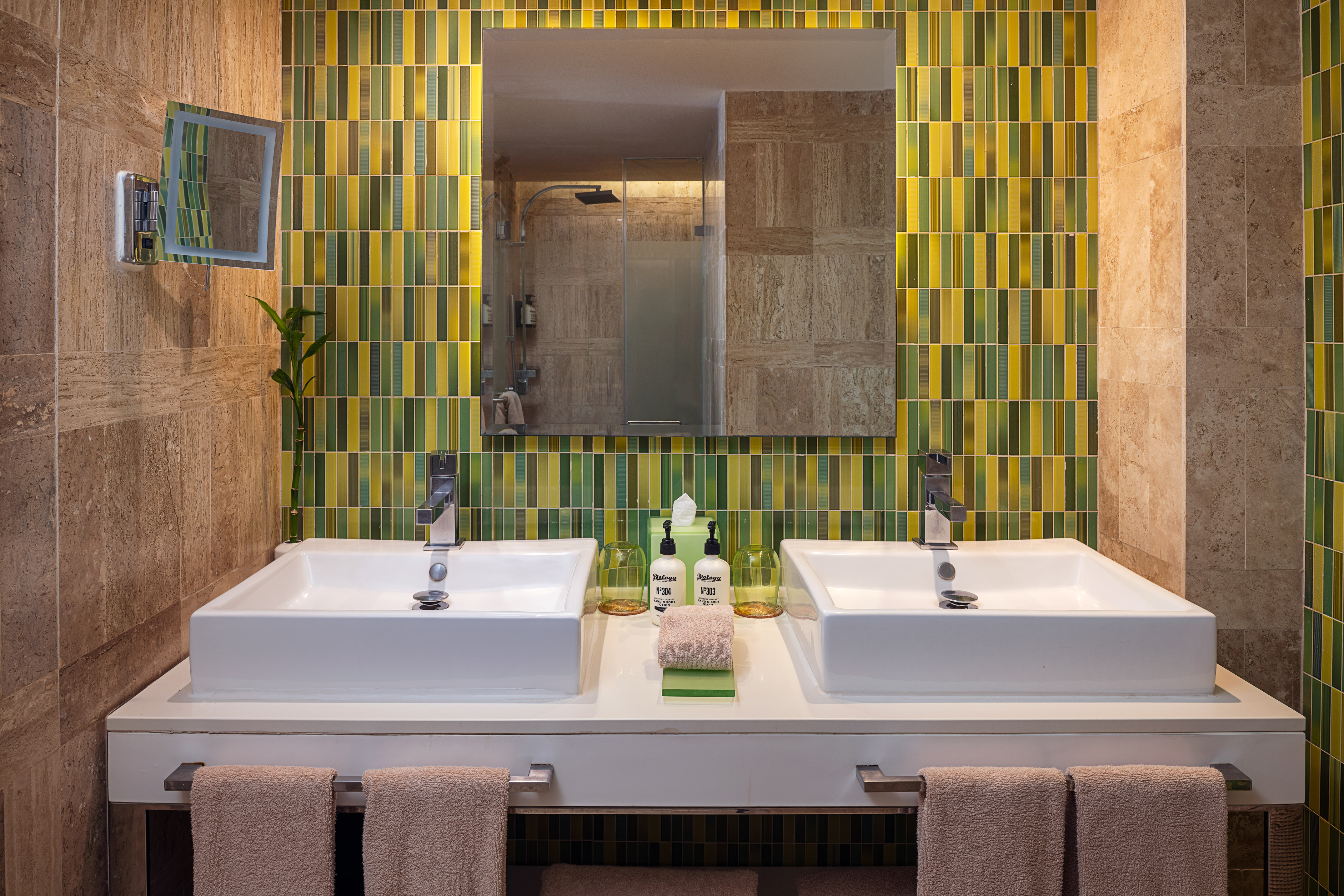 Modern bathroom with double sinks, green and yellow mosaic tiles, and large mirror.