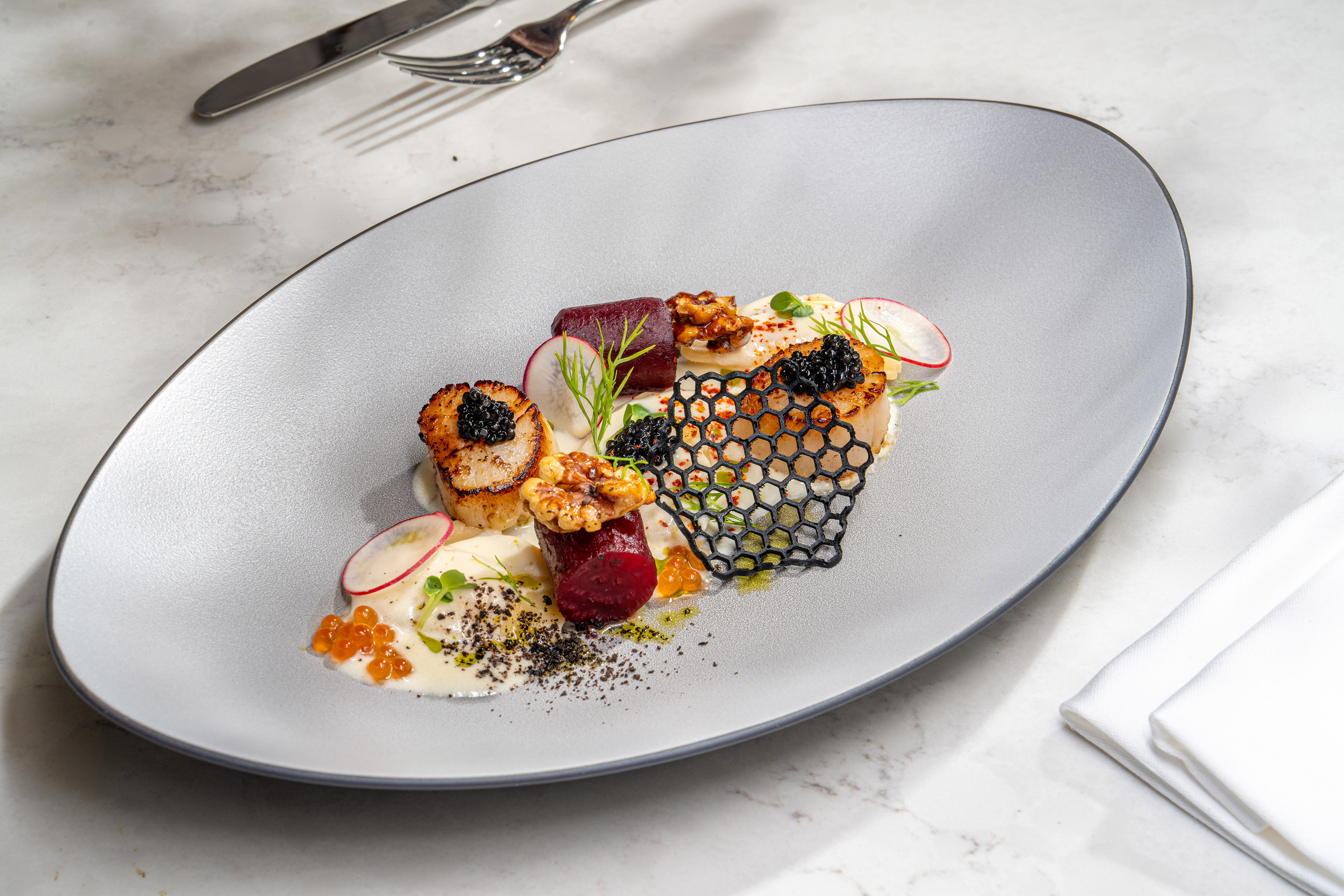 Gourmet seared scallops with black caviar, beetroot, walnuts, and radish.