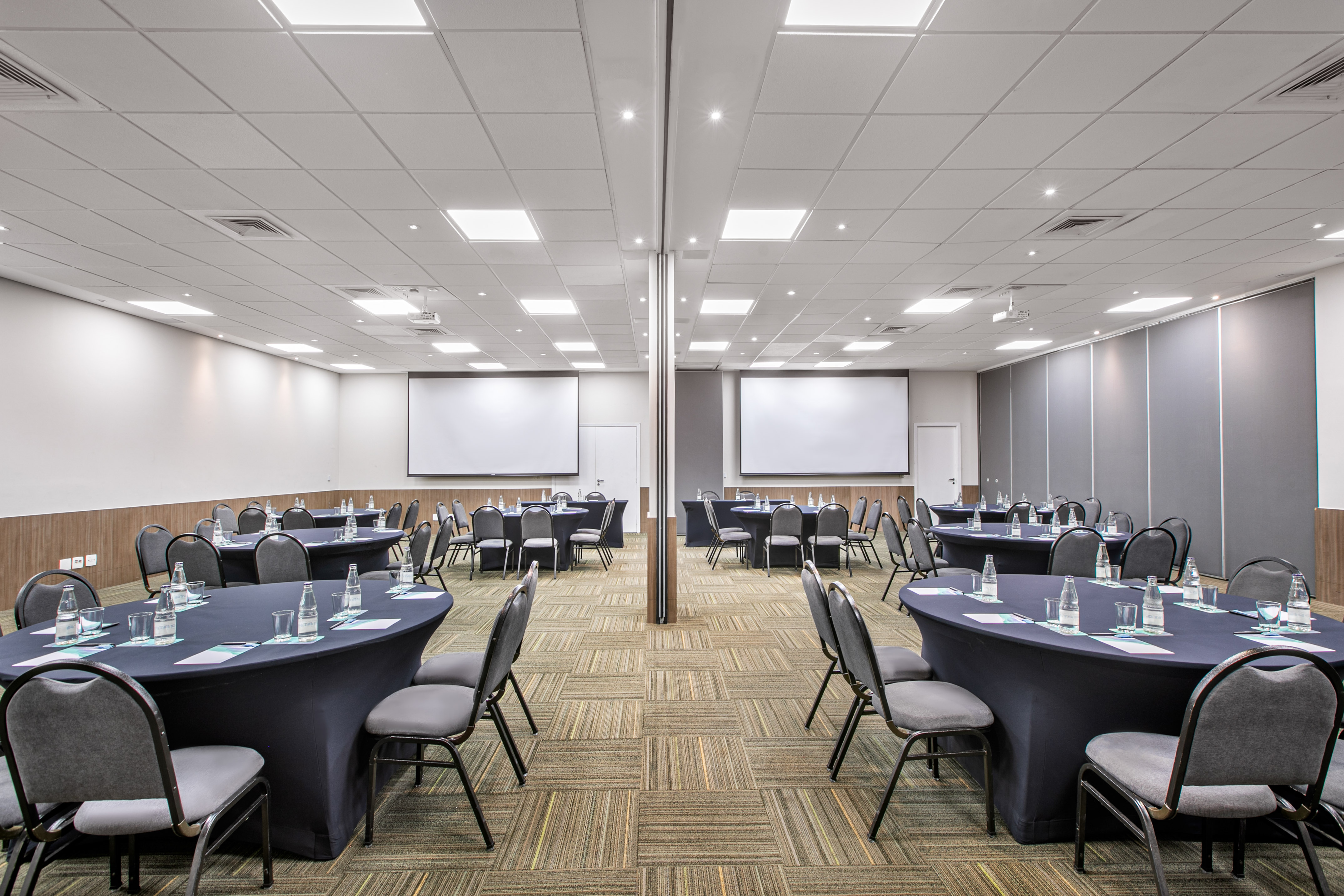 Conference room with oval tables, chairs, and dual projection screens.