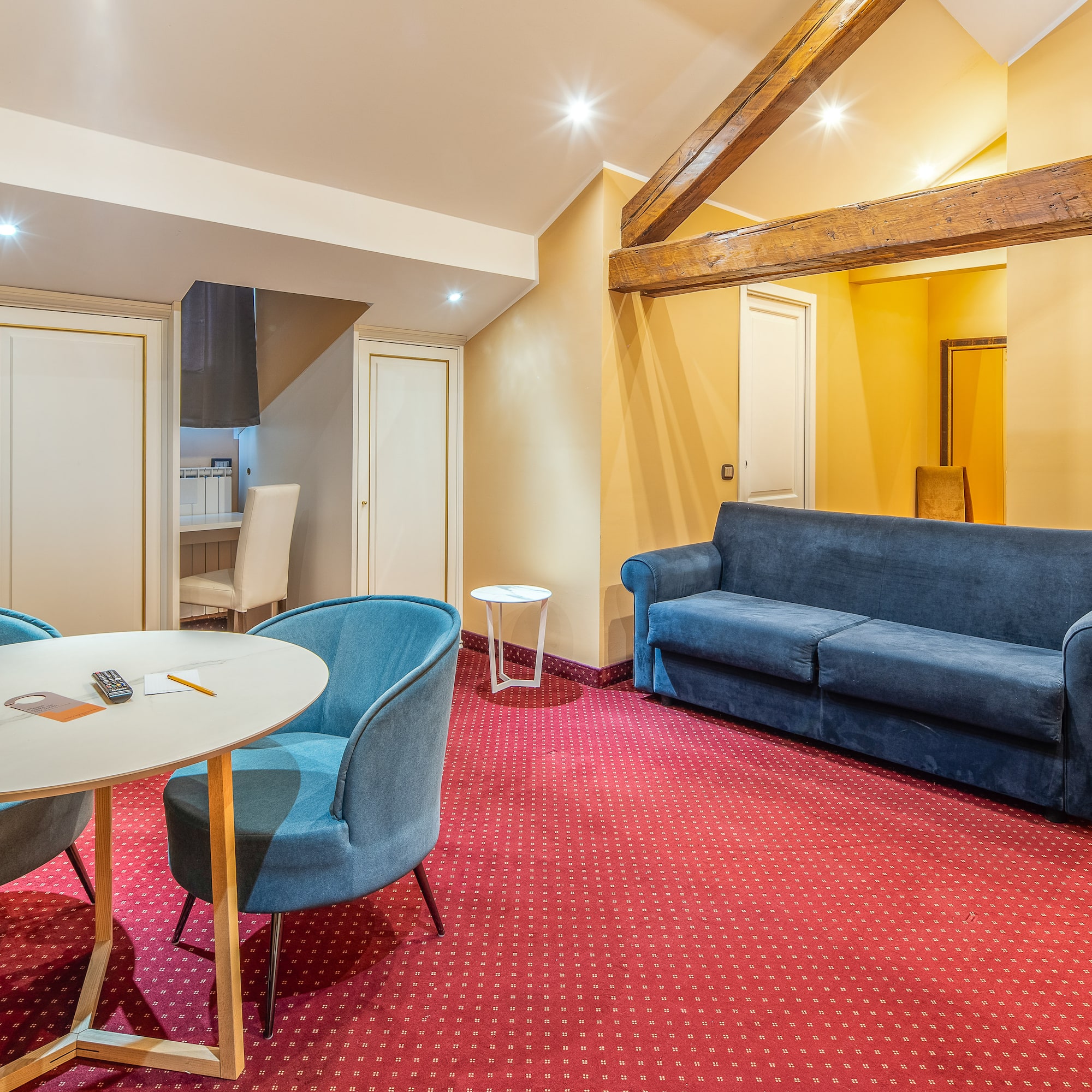 Hotel suite living room with red patterned carpet, blue sofa, and wooden beams.