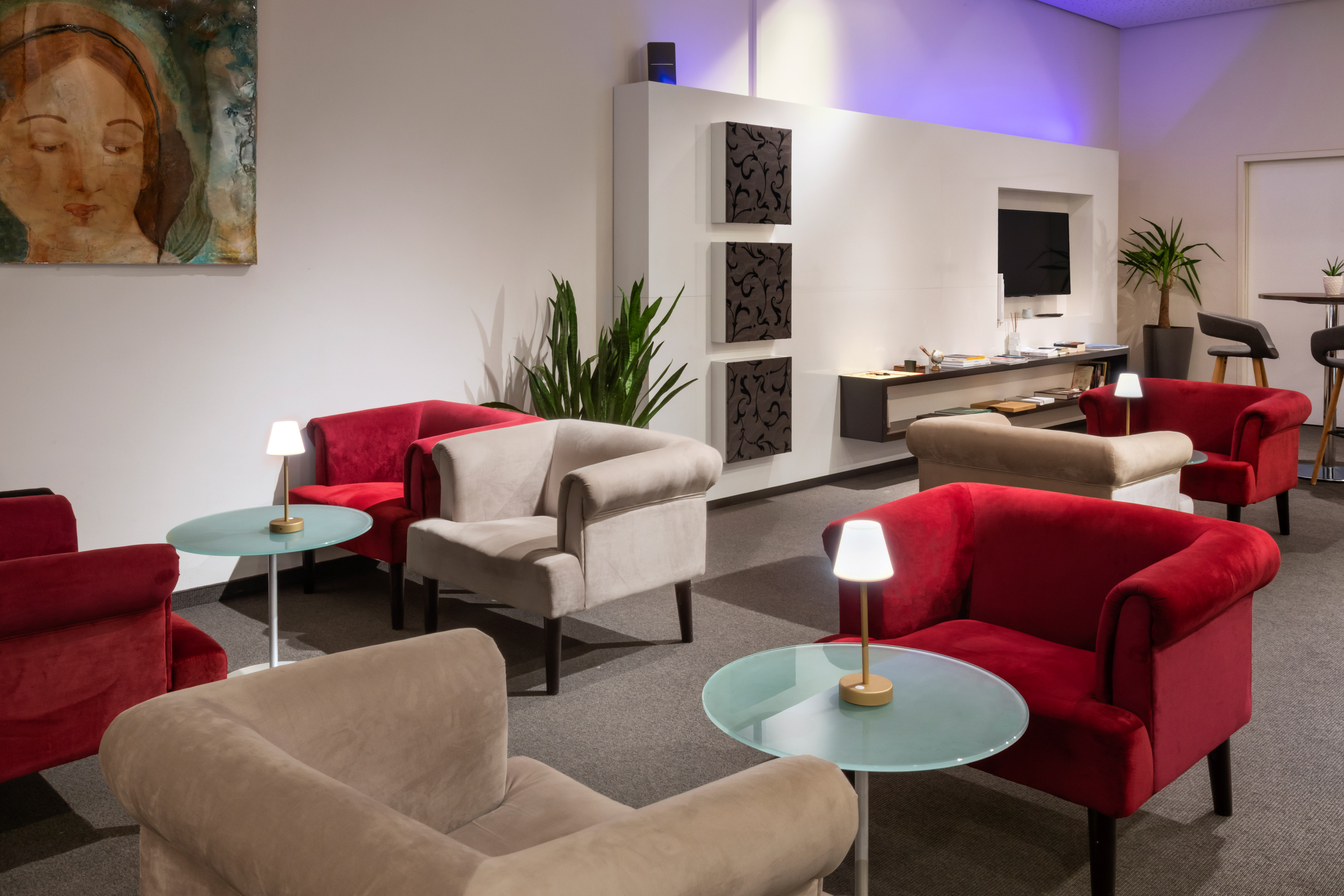 Hotel lounge with red and beige armchairs, glass tables, and ambient lighting.
