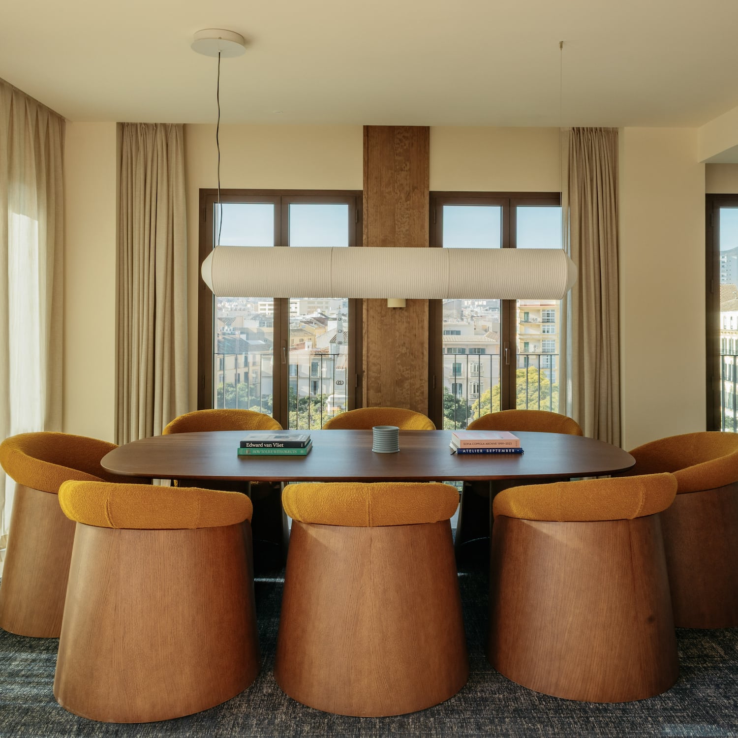 Modern dining room with oval wooden table, unique mustard chairs, city view.