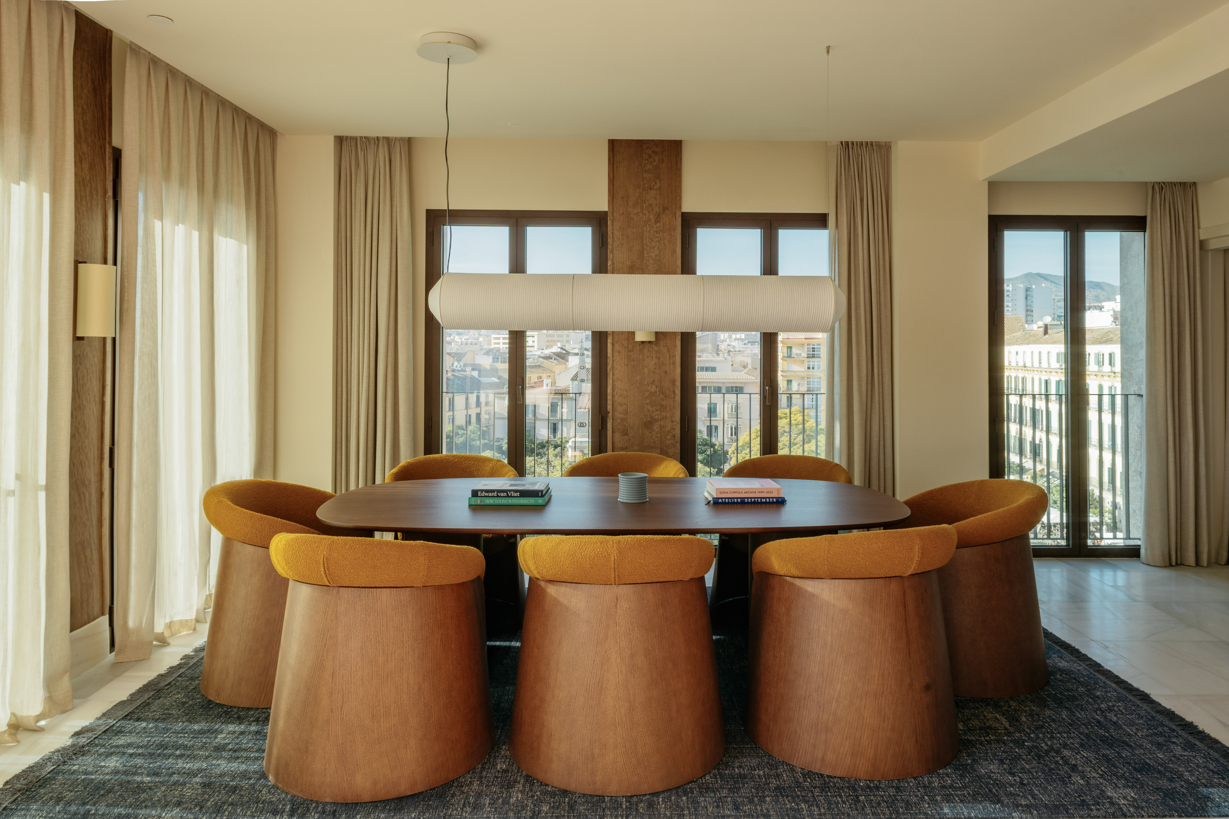 Modern dining room with oval wooden table, unique mustard chairs, city view.