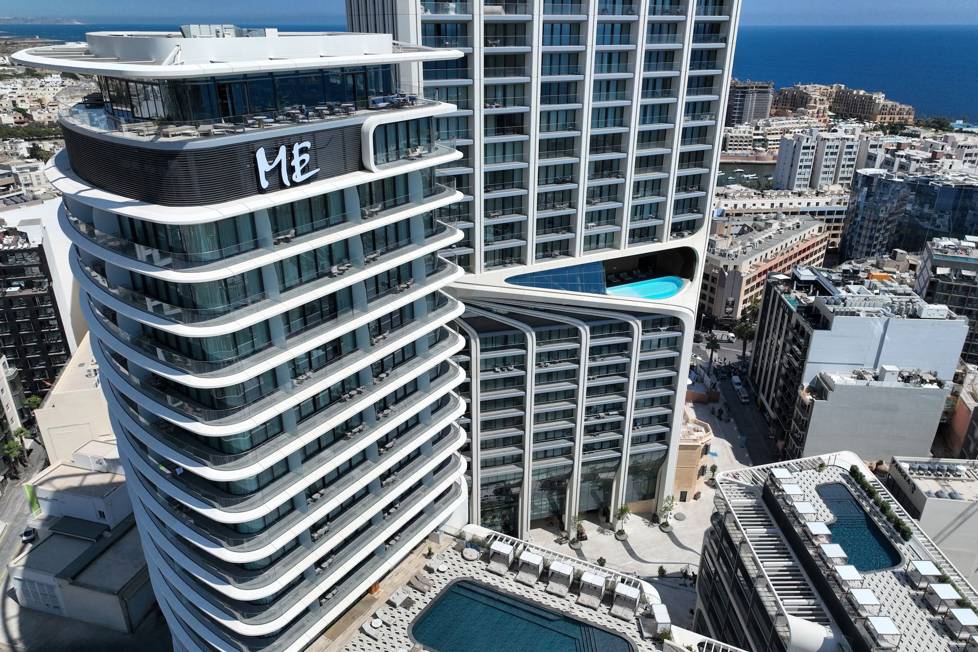 Modern ME hotel with curved architecture, rooftop pool, city, and sea views.